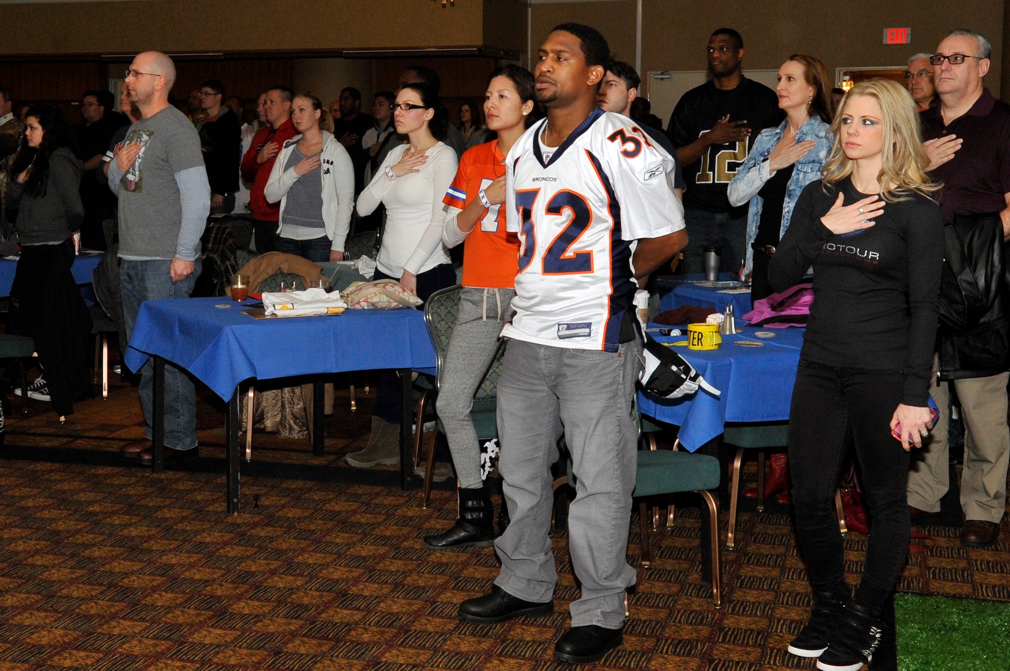 Dre Bly, National Football League alumnus, and members of the Misawa community stand for the national anthem before the kickoff of Super Bowl XLVIII at Misawa Air Base, Japan, Feb. 3, 2014. Bly and his fellow NFL alumni, along with two St. Louis Rams cheerleaders, gathered at the base club to watch the game with members of the base community. (U.S. Air Force photo by Airman 1st Class Zachary Kee)