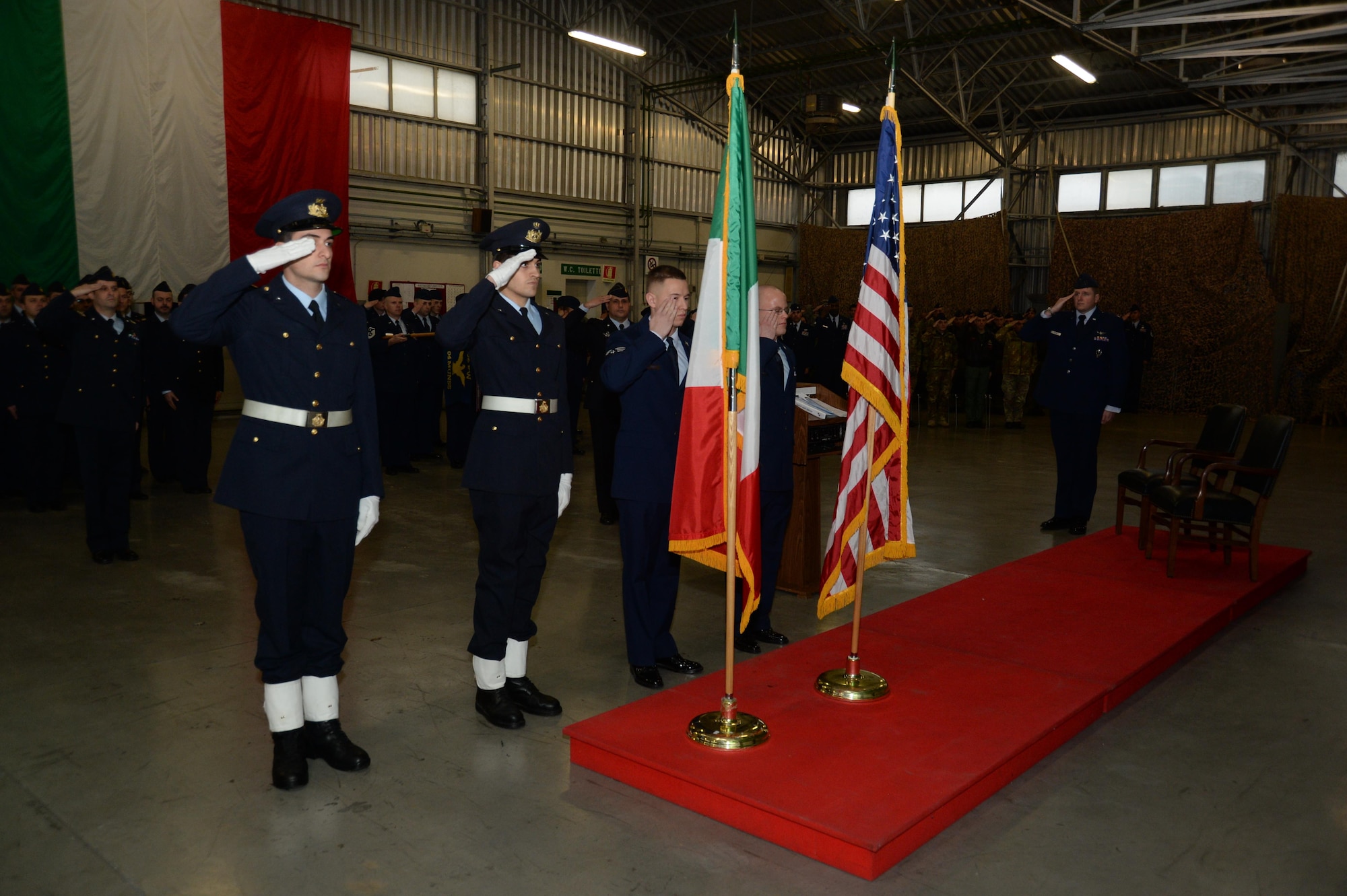 U.S. Air Force Airmen assigned to 704th Munitions Support Squadron and Italian Air Force Airmen assigned to 6th STORMO salute the Italian and U.S. flags during a ceremony in a hangar at Ghedi Air Base, Italy, Jan. 31, 2014. The ceremony paid tribute to the 50th anniversary of the Italian-American partnership established at Ghedi Air Base in December 1963.  (U.S. Air Force photo/Staff Sgt. Joe W. McFadden)
