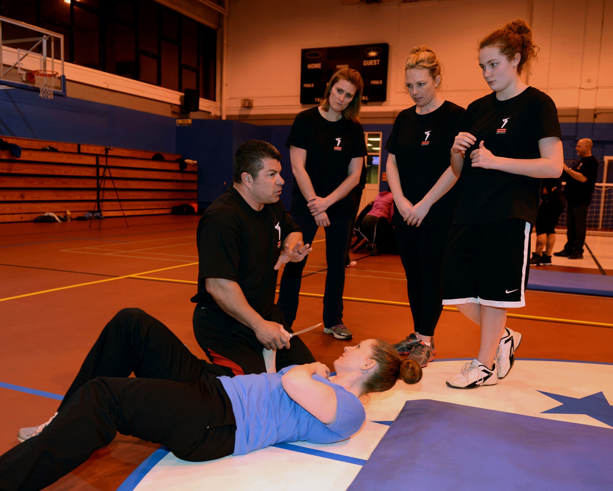 Rick Klein, kneeling, self-defense trainer, explains to Team Mildenhall women how to disarm an attacker after escaping from a knife attack Feb. 4, 2014, at the Northside Fitness Center on RAF Mildenhall, England. Klein, a former police officer, assists Linda Vu, women’s self-defense trainer, by acting as an attacker in several scenarios during Vu’s self-defense seminars. By substituting an attacker with himself, Klein allowed Team Mildenhall women to practice real-world techniques in a controlled environment. (U.S. Air Force photo by Airman 1st Class Preston Webb/Released)