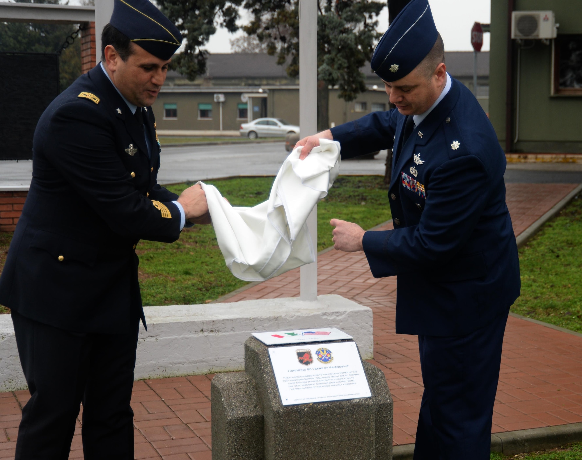 Italian Air Force Colonel Andrea Di Pietro, commander of 6th STORMO, and U.S. Air Force Lt. Col. James Soles, commander of the 704th Munitions Support Squadron, unveil a plaque near the U.S., Italian and NATO flagpoles outside during a rededication ceremony at Ghedi Air Base, Italy, Jan. 31, 2014. Both the 704th MUNSS and 6th STORMO carried out the rededication to honor the 50th anniversary of the Italian-American partnership at the air base.  (U.S. Air Force photo by Staff Sgt. Joe W. McFadden / Released)