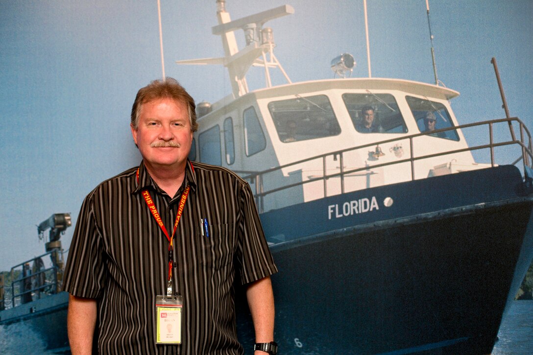 Brian Blake, senior lead of the coastal navigation team, Cost Engineering, was cited by Laureen Borochaner, chief, Engineering Division, for his loyalty to the Corps and specifically to the discipline of cost engineering. Blake stands in front of a photo of the survey boat Florida, on which he worked as a member of the Survey Branch upon his arrival at Jacksonville District in 1982.