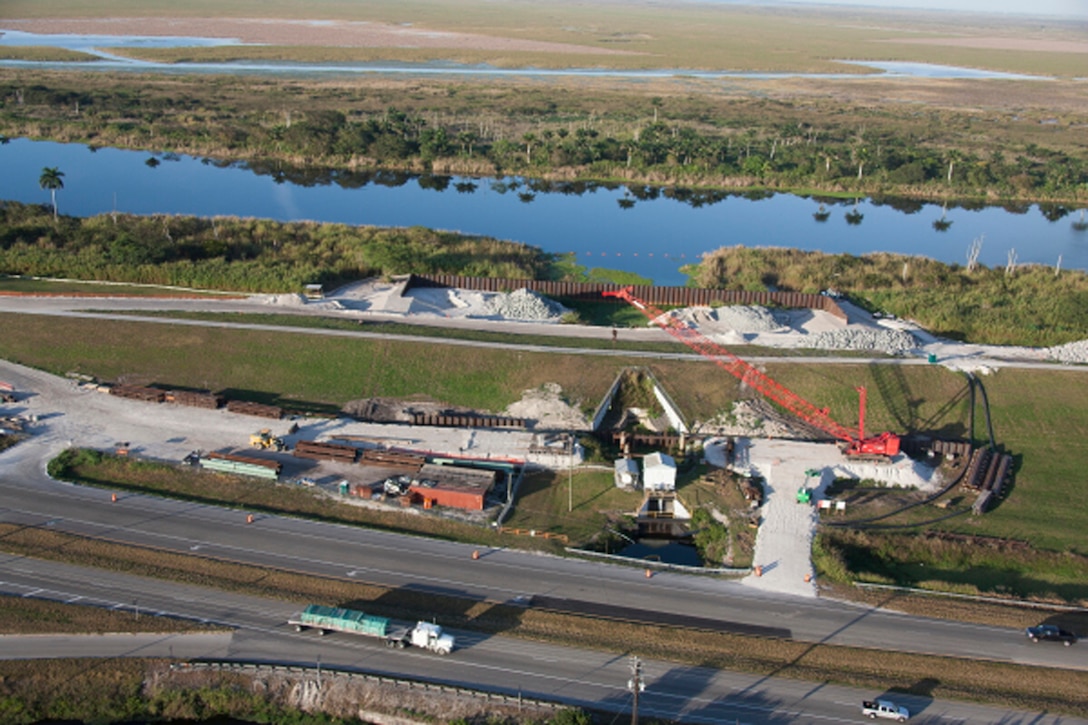 With traffic from U.S. 27 in the foreground, crews work on installing a temporary cofferdam at the Culvert 4A site near South Bay in December. The cofferdam, which must be robust enough to hold back Lake Okeechobee should it start rising, must be in place before the old culvert can be removed.