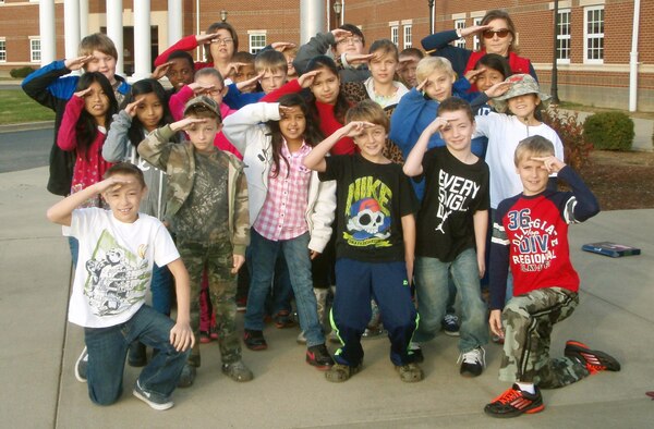 Fourth-grade students from Clear Creek Elementary School in Shelbyville, Ky., sent this photo of themselves in front of their school flag pole to Staff Sgt. Krome Raymond, a Kentucky Air National Guardsman from the Louisville-based 123rd Airlift Wing who is currently deployed to Afghanistan. The children and their teacher, Stephanie Herndon (back row, left), “adopted” Raymond, who sent them an American flag that they hoisted above the building. A traditional Air Guard member, Raymond is a full-time employee of the Shelby County School District, along with his wife, Dawn (back row, right). (Courtesy Photo)