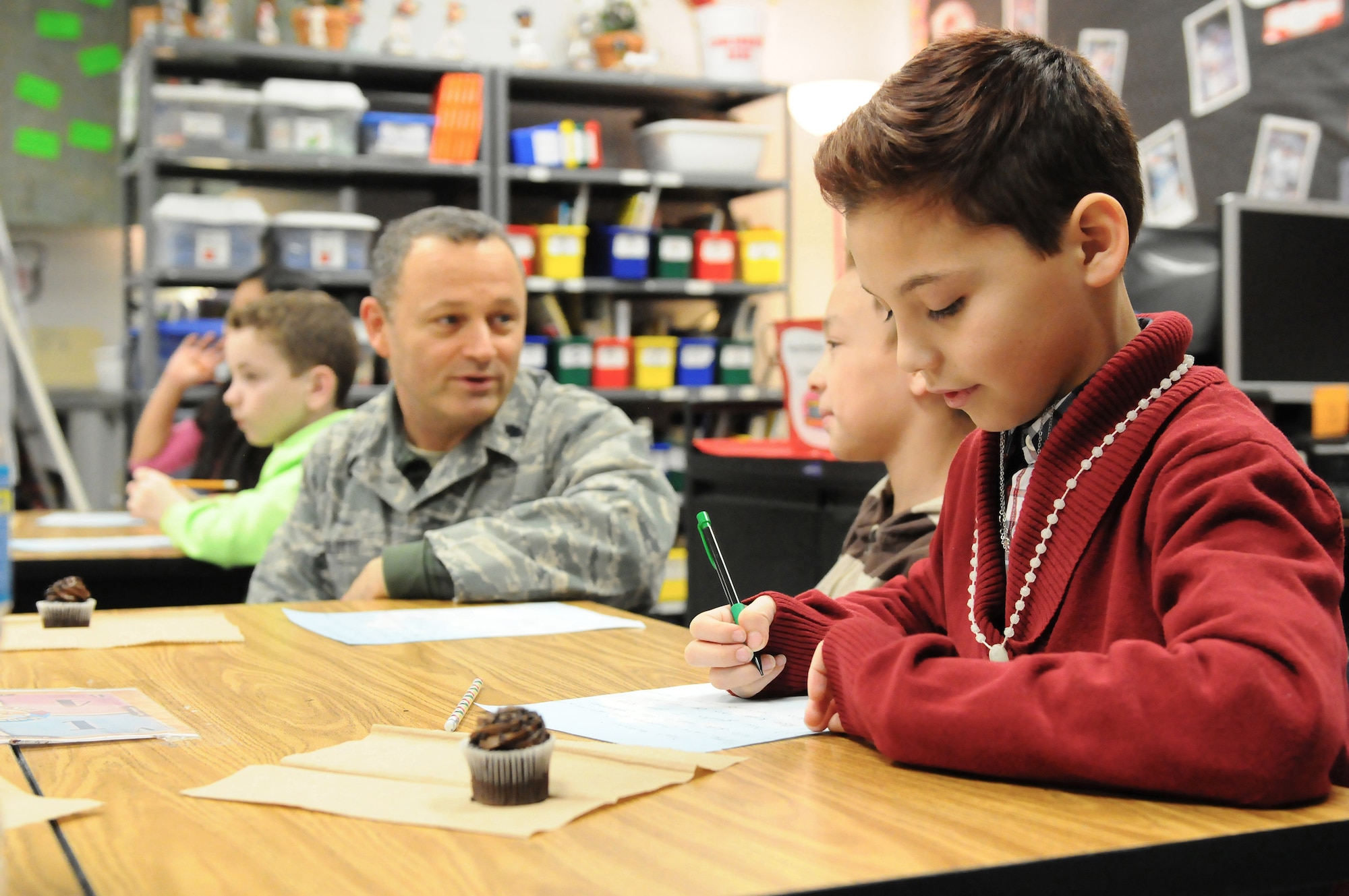 Austin Gozalez, a fourth-grade student at Clear Creek Elementary School in Shelbyville, Ky., writes a letter to Staff Sgt. Krome Raymond, a Kentucky Air National Guardsman who is deployed to Afghanistan, as Raymond's supervisor, Lt. Col. Armand Bolotte, looks on during a classroom visit Jan. 9, 2014. Gonzalez and his classmates have “adopted” members of the Louisville-based 123rd Airlift Wing for the duration of their deployments, sending them letters and snacks. (U.S. Air National Guard photo by Staff Sgt. Vicky Spesard)