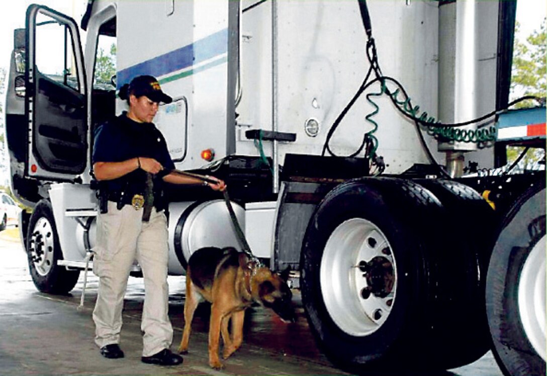 Cpl. Tonette Gezzi, civilian K-9 handler, Marine Corps Police Department, MCLB Albany, and her K-9 partner inspects a truck, recently.