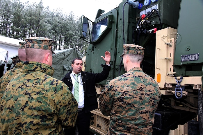 Jaspal Brar (center), an engineer in Marine Corps Systems Command’s Systems Engineering, Interoperability, Architectures and Technology—or SIAT—talks to Marines about the Medium Tactical Vehicle Replacement Auxiliary Power Unit during a technology demonstration Feb. 5 in Quantico, Va. The 10-kilowatt APU is mounted behind the cab of the MTVR and allows various electrical functions to run while the main vehicle engine is off. Brar is leading MCSC’s initiative to evaluate the feasibility and potential energy savings of the MTVR APU. 