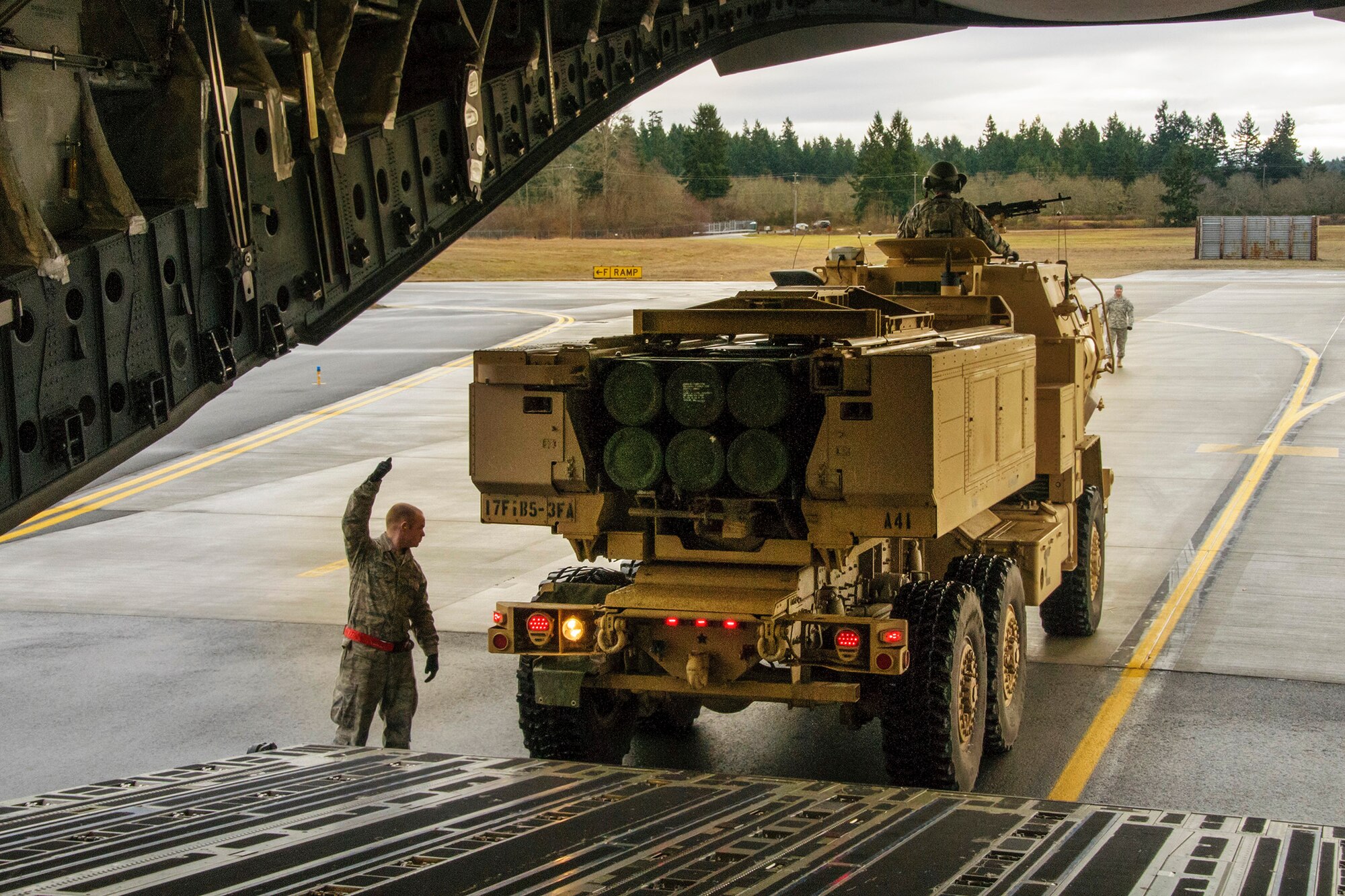 An aerial port specialist from the 62nd Airlift Wing directs a 17th Fires Brigade vehicle onto a C-17 Globemaster III aircraft, Jan. 31. The loading was part of an Air Force and Amry operation to test fire the M142 High Mobility Artillery Rocket System. (U.S. Air Force photo by Jake Chappelle)