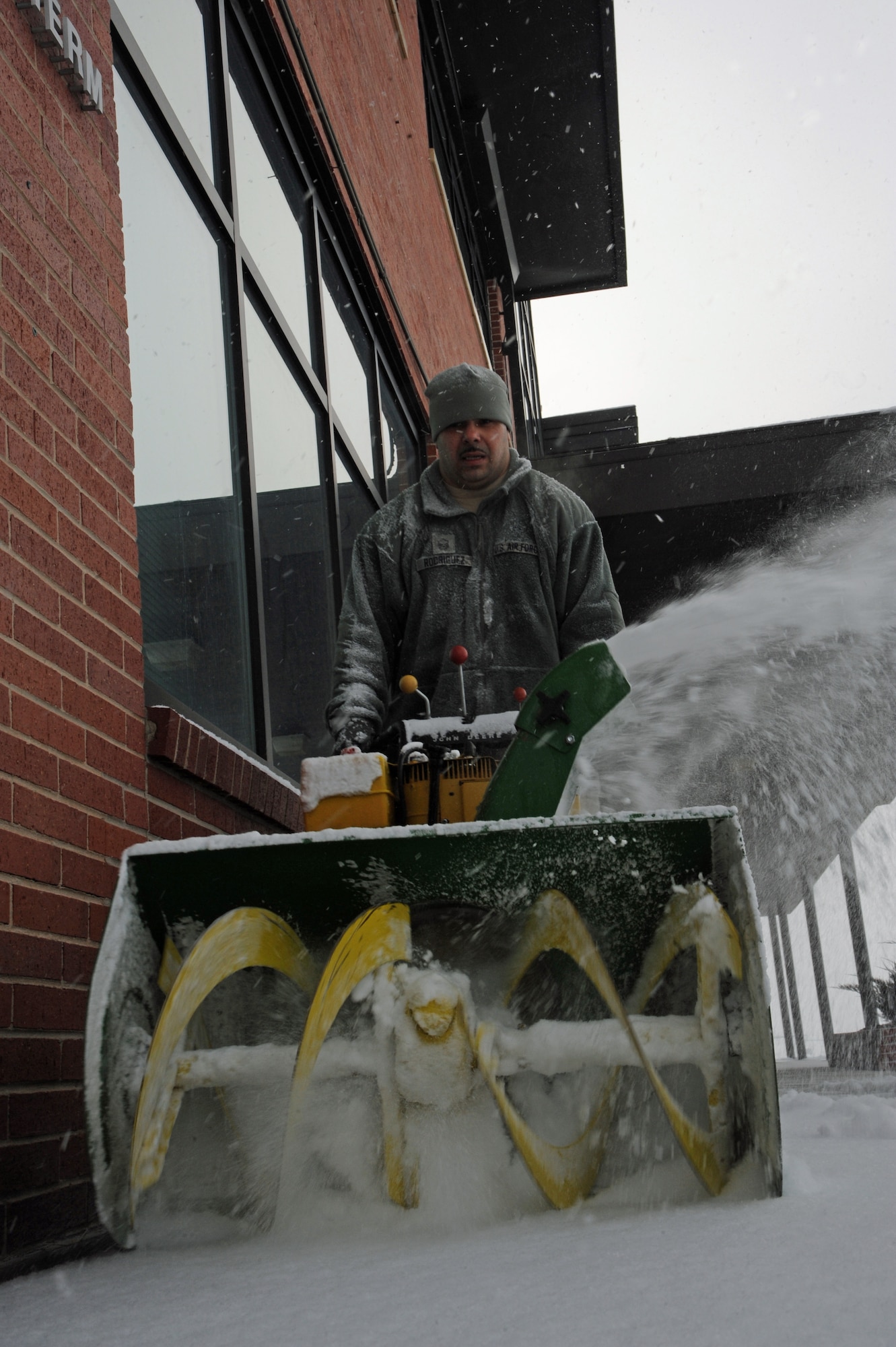 PETERSON AIR FORCE BASE, Colo. -- Master Sgt. Juan Rodriguez, 21st Space Wing Protocol NCO in charge, uses a snow thrower to remove snow from the walkway to protocol from the flightline Feb. 4. The 21st Civil Engineer Squadron relies on building managers, augmentees and contractors to clear the walkways on base during and after snow. (U.S. Air Force photo/Staff Sgt. Jacob Morgan)