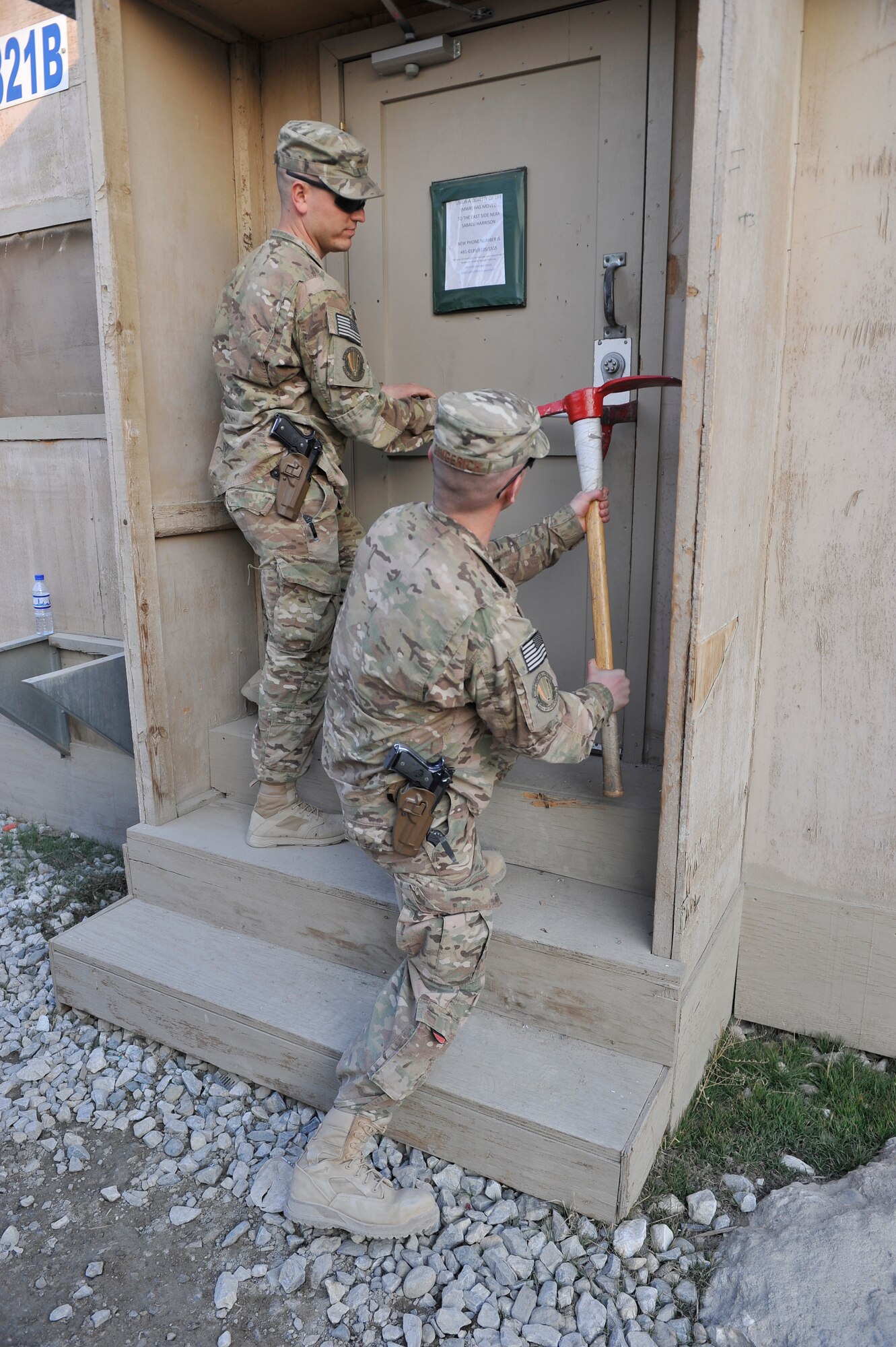 U.S. Air Force Staff Sgt. Wade Ferry holds a tool called a halligan beside a door latch while Staff Sgt. Rueben Gingerich uses his mattock to pound it in to a gap on the door of a B-hut at Bagram Airfield, Afghanistan, Jan. 30, 2014. Ferry and Gingerich are members of a team responsible for identifying buildings to be torn down. One of their last tasks is to open all doors to ensure the building is empty before final demolition begins.(U.S. Air Force photo by Senior Master Sgt. Gary J. Rihn/Released)