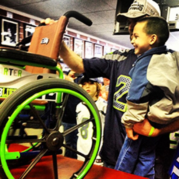 Karter Lee smiles as he sees the "12" on the back of his new Seahawk themed wheelchair Jan. 25 in Mill Creek, Wash. The wheelchair was put together for him by a team of volunteers including Tech. Sgt. Shawn Walker, 446th Civil Engineer Squadron firefighter, and his girlfriend Jessica Kuehne, who initated the project after seeing a story Lee's mother wrote on Facebook. (Photo courtesy of Tech. Sgt. Shawn Walker)