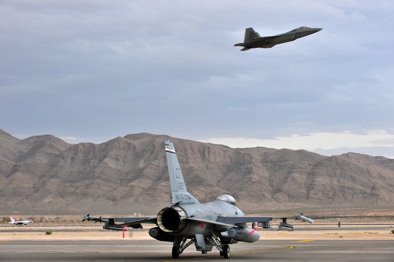 An F-16 Fighting Falcon fighter jet from the 120th Fighter Squadron at Buckley Air Force Base, Colorado Air National Guard, taxis for a training mission during Red Flag 14-1, as an F-22 Raptor from the 94th Fighter Squadron located at Joint Base Langley-Eustis, Virginia, takes off at Nellis Air Force Base, Nev., Jan. 30, 2014. Combat units come together from the United States and its allied countries to engage in realistic combat training scenarios within Nellis’ 2.9 million acre Test and Training Range Complex. (U.S. Air National Guard photo/Tech. Sgt. Wolfram M. Stumpf)