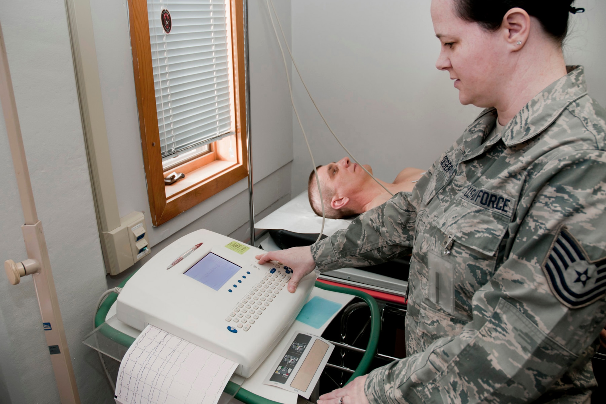 Tech. Sgt. Stephanie Ploeger (front right) hooks Master Sgt. Mike Johnson (back middle) up to an electrocardiogram (EKG) machine for simulated testing on his heart in the exam room of the 132nd Fighter Wing (132FW) Medical Facility, Des Moines, Iowa on February 7, 2014.  (U.S. Air National Guard photo by Staff Sgt. Linda K. Burger/Released)
