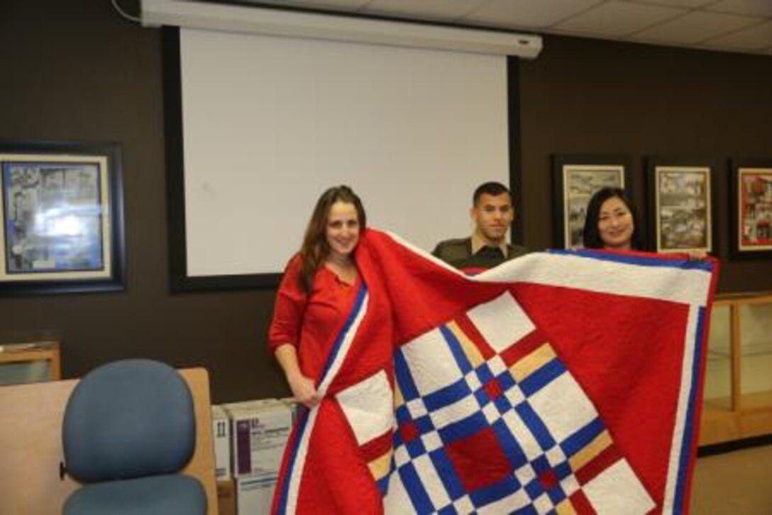 (From left to right) Kelly Smith, quilter with the Quilts of Valor, Cpl. Samuel Ribeiro, noncommissioned officer in charge of the adjutant section on Marine Corps Logistics Base Barstow, Calif., and Cathy Choi, also a quilter, pose for a photo with the quilt the women made for him, Feb. 7.


