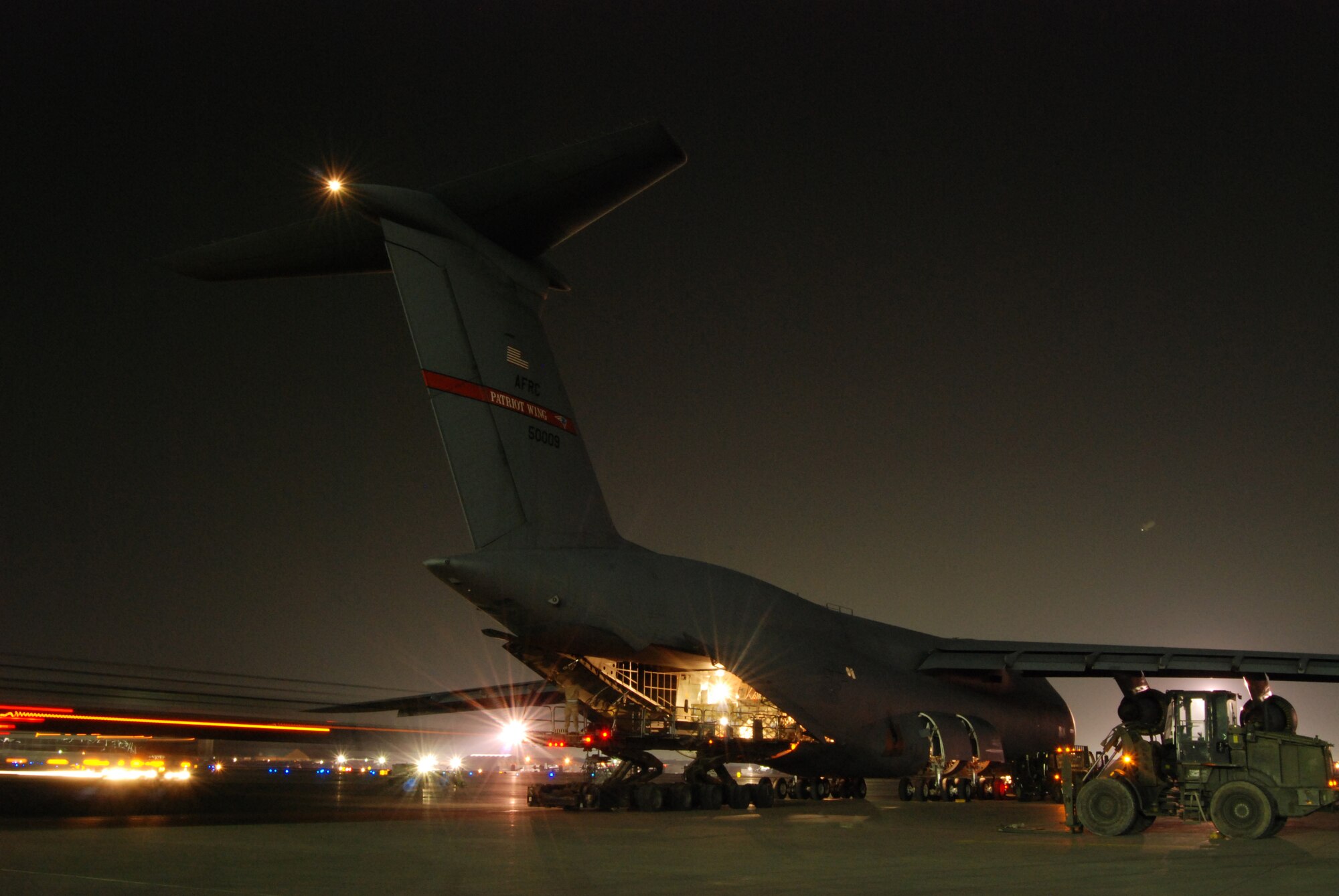 An Airman marshals a Tunner 60K Loader into position behind a C-5B Galaxy at Bagram Airfield, Afghanistan, Feb. 11, 2014. Aerial port Airmen off-loaded multiple pallets of cargo from the C-5B, which is the Department of Defense’s largest military aircraft. (U.S. Air Force photo by Capt. Brian Wagner/Released)