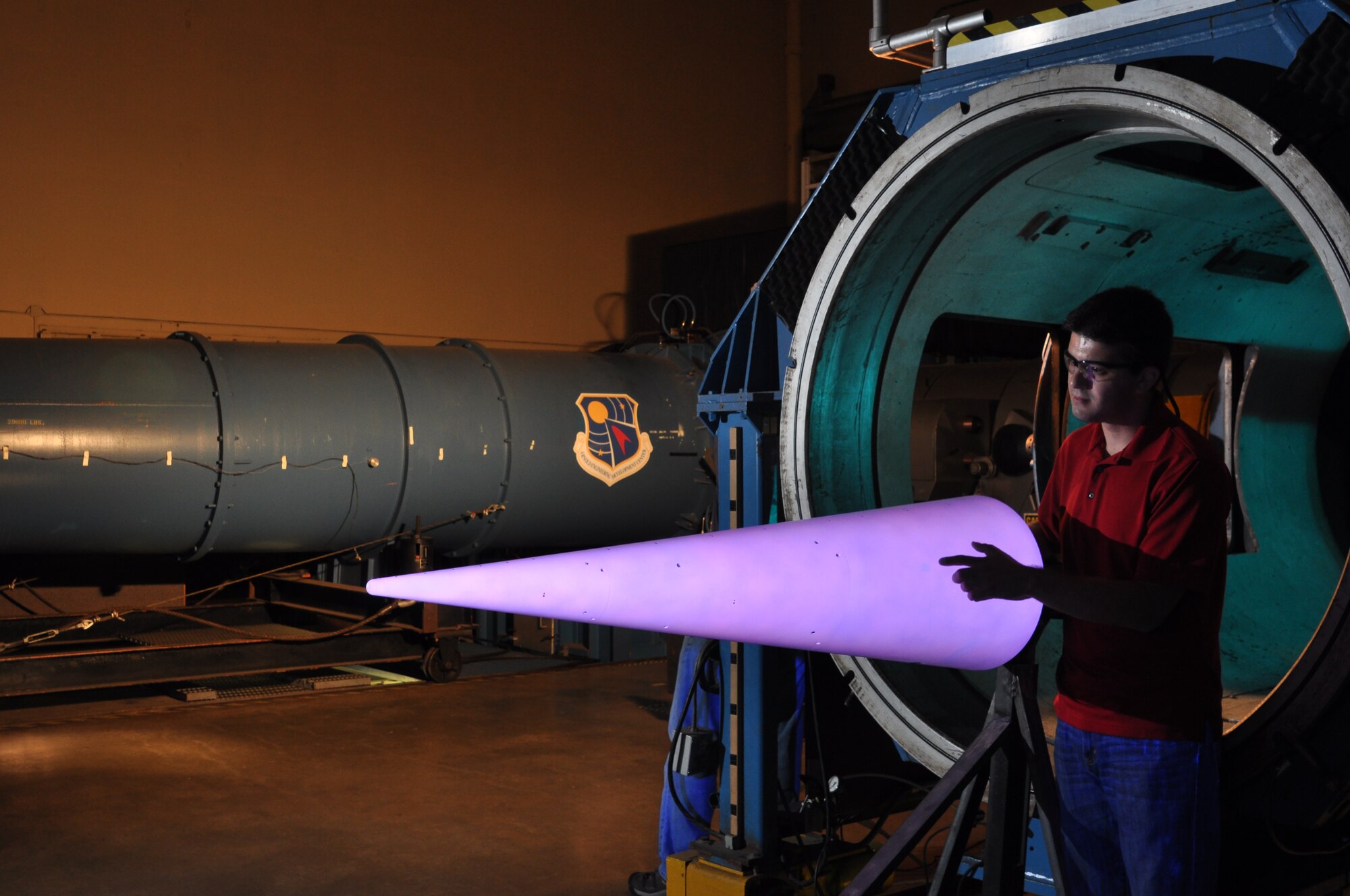Air Force Project Engineer and Purdue University graduate student George Moraru examines the illuminated temperature sensitive paint (TSP) coating on the large, 7-degree cone prior to the test program. The testing is performed under the Test Resource Management Center (TRMC) and the Air Force Office of Scientific Research (AFOSR) funded Hypersonic Center of Testing Excellence (CoTE). (Photo by Michael Smith)