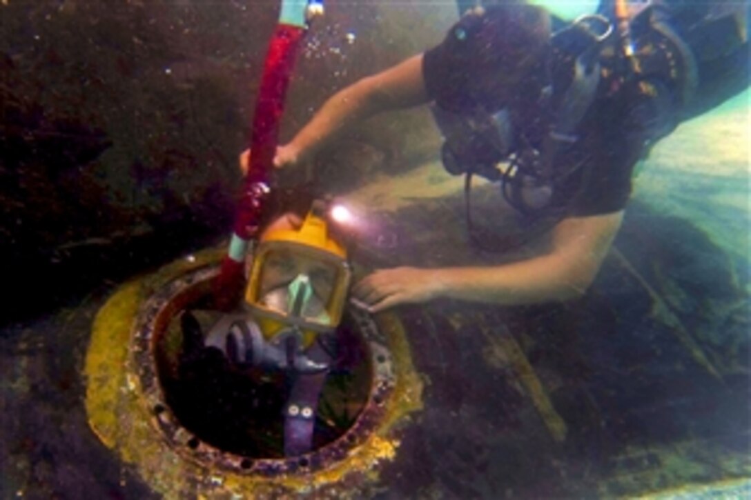 U.S. Navy Petty Officers 3rd Class Erik Clark, right, helps Jeremy Redgrift exit the mud tank aboard the attack submarine USS Key West in Polaris Point, Guam, Feb. 11, 2014. Clark and Redgriff, divers assigned to the submarine tender USS Frank Cable, are conducting preventive and corrective maintenance. The Cable, forward deployed to the island of Guam, conducts maintenance and support of submarines and surface vessels in the U.S. 7th Fleet area of responsibility.