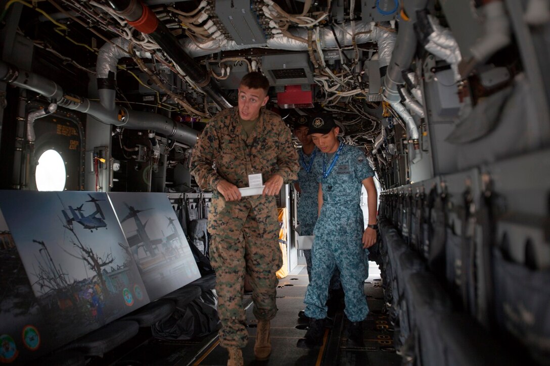 Lance Cpl. Andrew M. Weis escorts members of the Royal Singapore Air Force through an MV-22B Osprey Feb. 11 at the Changi Exhibition Center in Singapore. The Osprey was on exhibit in the static display area of the Singapore International Airshow 2014 and gave show-goers the opportunity to walk around inside the aircraft and even sit in the cockpit. The Singapore Air Show 2014 helps build stronger relations between the U.S. and Singapore, as well as among the international community. The event promotes military to military discussions on aircraft and equipment, which enables greater interoperability of aviation platforms, and furthers international military relationships and cooperation. The U.S. is committed to maintaining peace and stability in the region, and this event demonstrates a focus of the U.S. rebalance to the Asia-Pacific region. Weis is a tiltrotor mechanic with Marine Medium Tiltrotor Squadron 262, Marine Aircraft Group 36, 1st Marine Aircraft Wing, III Marine Expeditionary Force, and the Osprey is with VMM-262. (U.S. Marine Corps photo by Cpl. Lena Wakayama/Released)