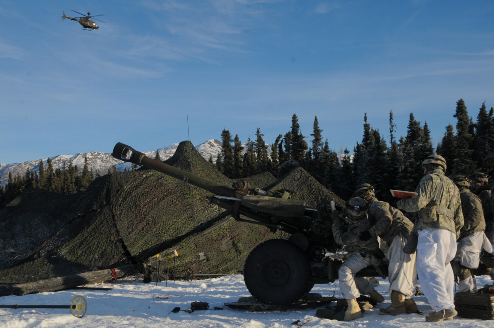 Cannon crewmembers with the 2nd Battalion, 377th Parachute Field Artillery Regiment, certify in crew drills as an OH-58 Kiowa Warrior helicopter flies overhead Jan. 31 at JBER. The Spartan Brigade took full advantage of the pleasant weather conditions to train during a nine-day field training exercise designed to further validate its readiness as the Army’s only active airborne brigade in the Asia-Pacific Theater. (U.S. Army photo/Staff Sgt. Jeffrey Smith)