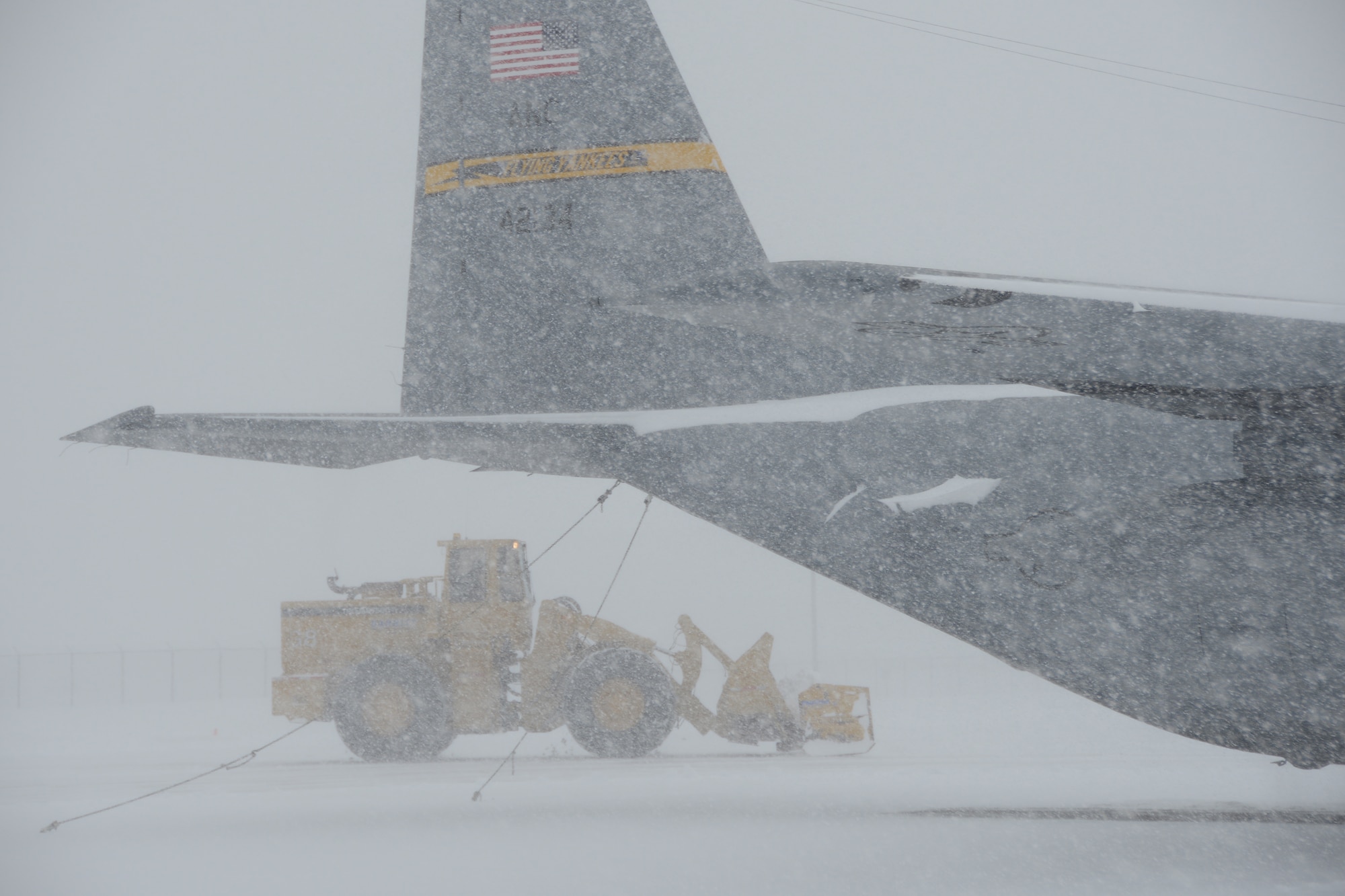 A C-130H aircraft assigned to the 103rd Airlift Wing parked at Bradley Air National Guard Base, East Granby, Conn., as a plow works to clear the flightline of the rapidly accumulating snow from a nor’easter Feb. 13, 2014. More than 200 Airmen reported to work here and at the Orange Air National Guard Station, ready to answer the call in the event the state required assistance during the height of the storm.  (U.S. Air National Guard photo by Maj. Bryon M. Turner)