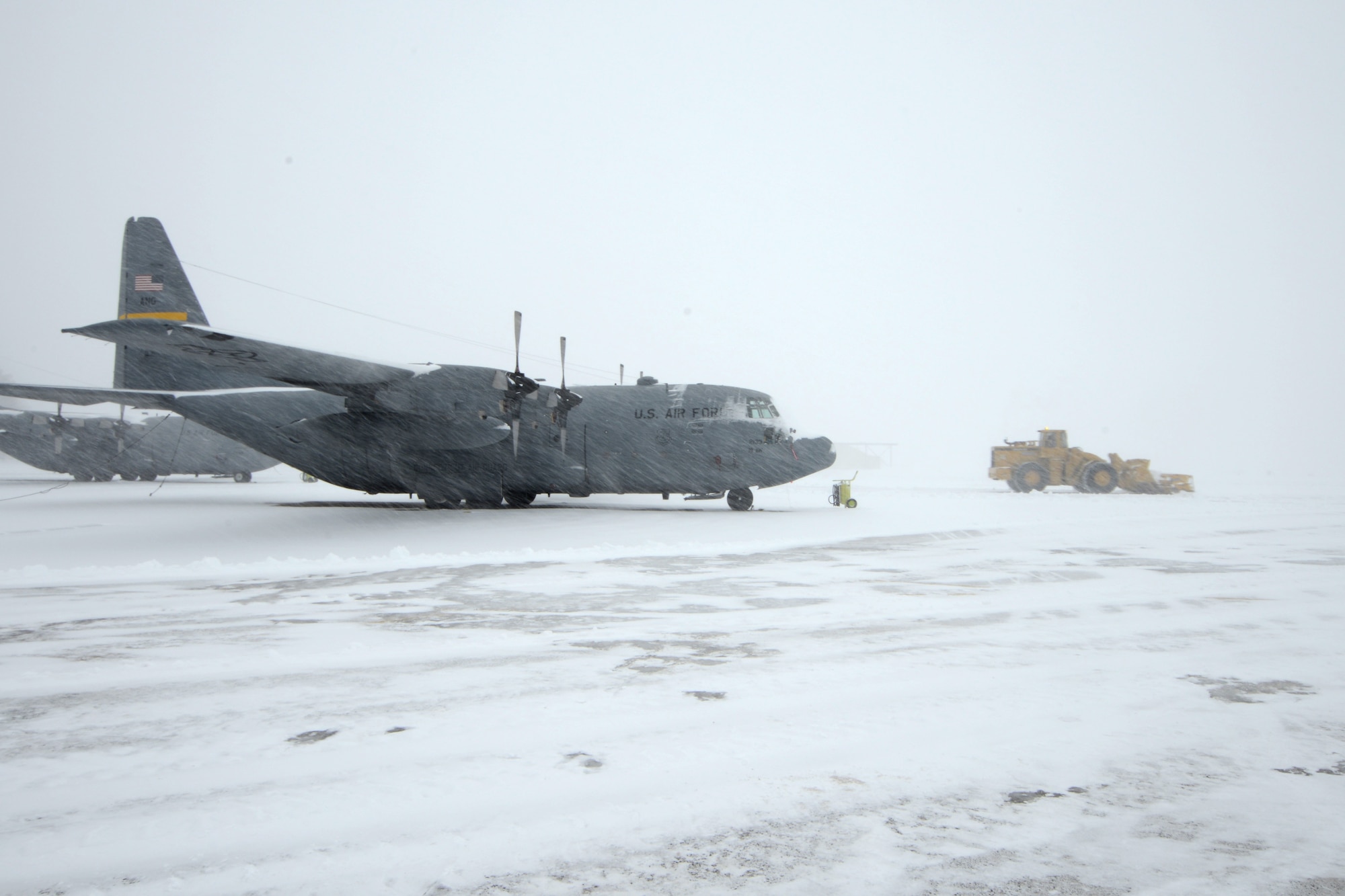 A C-130H assigned to the 103rd Airlift Wing in East Granby, Conn. weathers the storm Feb. 13, 2014, as more than a half dozen machines from the adjacent Bradley International Airport work to clear the rapdily accumulating snow from the aircraft ramp at Bradley Air National Guard Base, East Granby, Conn.  (U.S. Air National Guard photo by Master Sgt. Erin McNamara)