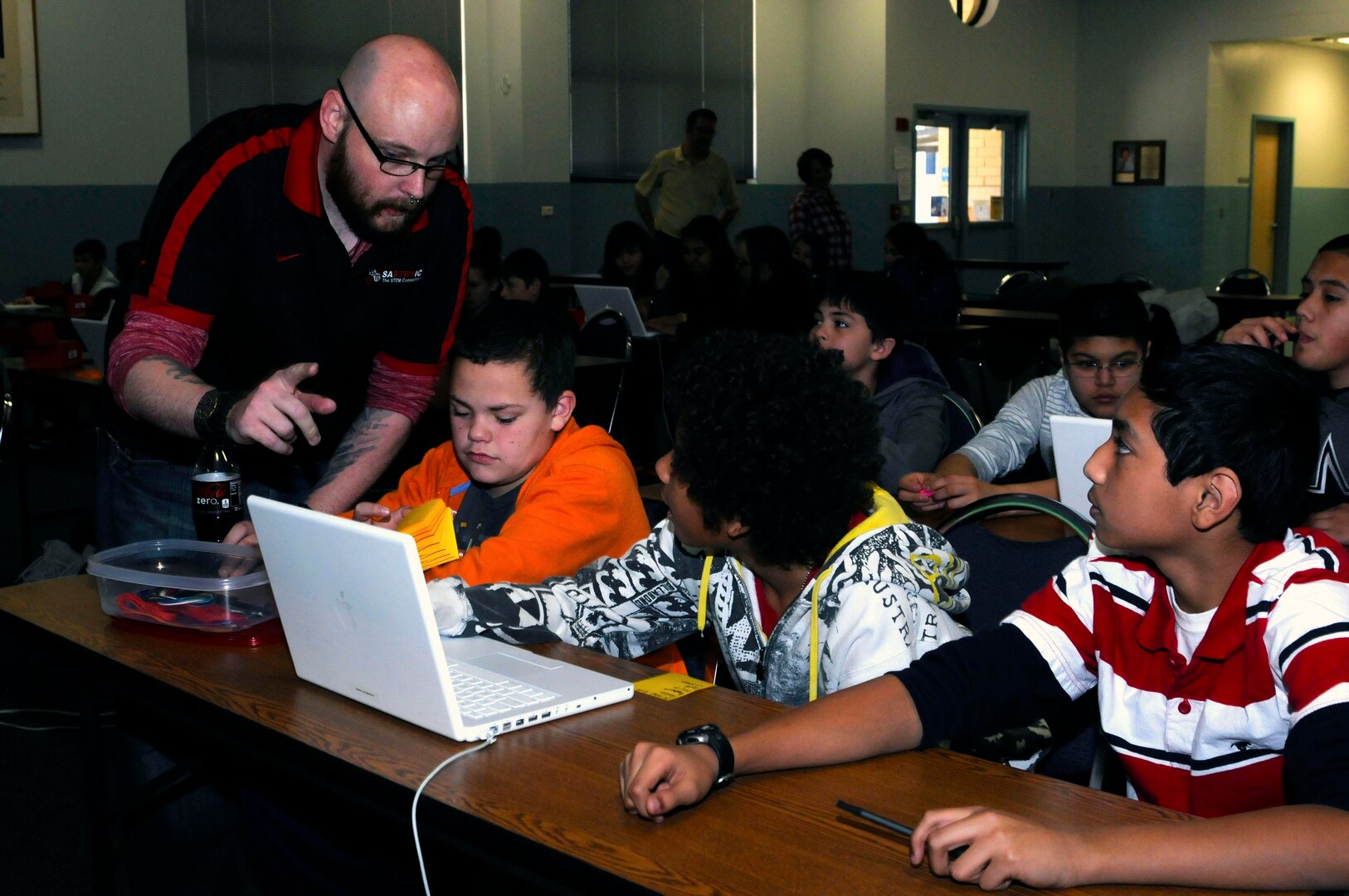 Mark Burnett, an instructor with the Geekbus program, helps students navigate a software program during a visit to Lackland Elementary School Jan. 29. During the classroom portion of the visit, students learned problem solving techniques through video game design and creating controllers from cardboard and metal tape. The Geekbus travels to schools in San Antonio to get students interested in science, technology, engineering and mathematics.