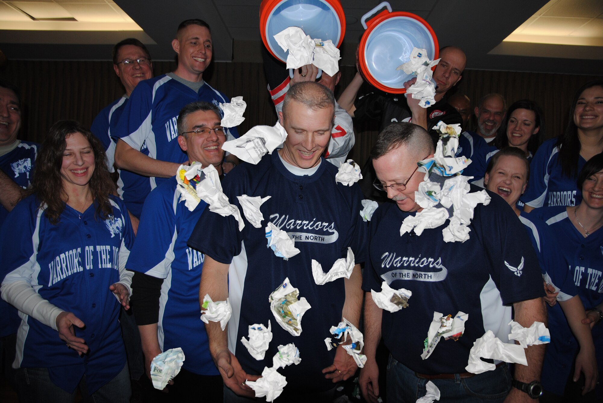 Grand Forks Air Force Base 2013 Annual Awards Committee members Senior Master Sgts. Troy Blanchard and Michael Knox, dump two five-gallon coolers full of crumpled paper on Col. Paul Bauman, 319th Air Base Wing commander and 319th ABW command chief, Chief Master Sgt. David Duncan, during the 2013 Grand Forks Air Force Base Annual Awards Feb. 7, 2014, at Northern Lights Club on Grand Forks AFB, N.D. The surprise was meant to symbolize the congratulatory Gatorade shower that football coaches typically get from their teams after a championship win.(U.S. Air Force photo/Staff Sgt. Luis Loza Gutierrez) 
