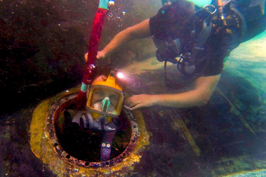U.S. Navy Petty Officers 3rd Class Erik Clark, right, helps Jeremy Redgrift exit the mud tank aboard the attack submarine USS Key West in Polaris Point, Guam, Feb. 11, 2014. Clark and Redgriff, divers assigned to the submarine tender USS Frank Cable, are conducting preventive and corrective maintenance. The Cable, forward deployed to the island of Guam, conducts maintenance and support of submarines and surface vessels in the U.S. 7th Fleet area of responsibility.