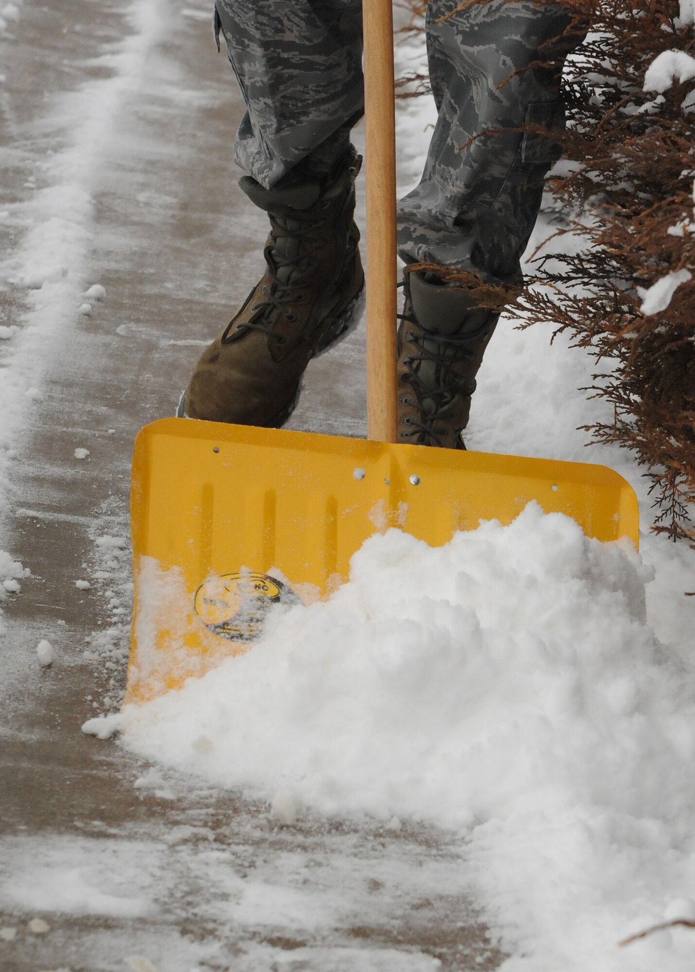 Snow piles up in the front of a shovel as an Airman clears a sidewalk for pedestrians. Even with colder temperatures, Airmen across base spend many hours bearing the cold to clear sidewalks and roads, which are essential for safe travel. (U.S. Air Force photo/Senior Airman Cortney Paxton)