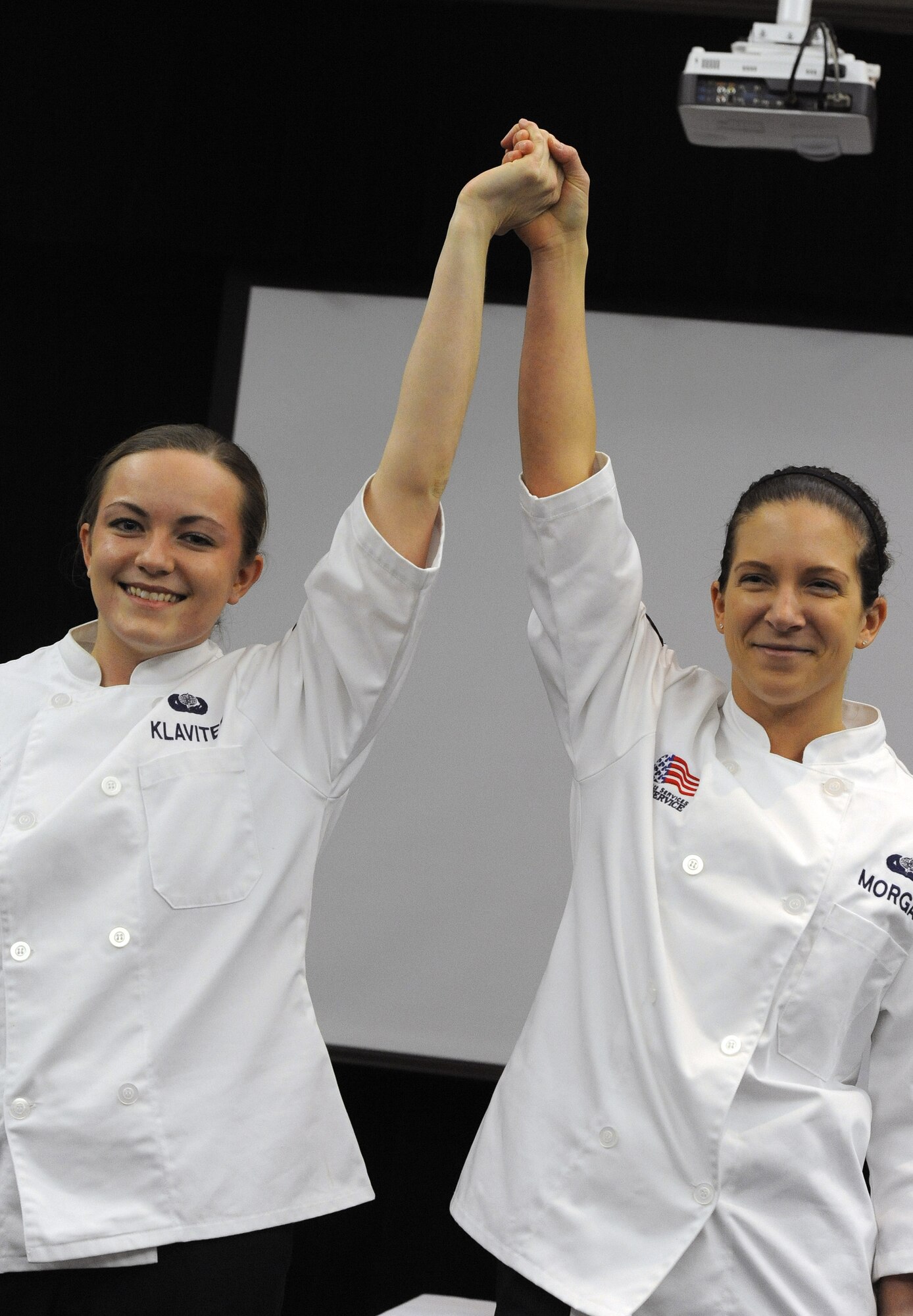Airmen 1st Class Amy Klaviter and Elizabeth Morgan, food services specialists from the 509th Force Support  Squadron, share a bow after providing a mission brief to Hennessy Team evaluators at Mission’s End at Whiteman Air Force Base, Mo., Feb. 5, 2014. The Hennessy team visits different dining facilities throughout the Air Force and inspects a variety of items to determine the best food service in the Air Force. The 509th FSS was named the 2013 John L. Hennessy Trophy winner, which is awarded to the Air Force’s best food service unit. (U.S. Air Force photo by Staff Sgt. Nick Wilson/Released)
