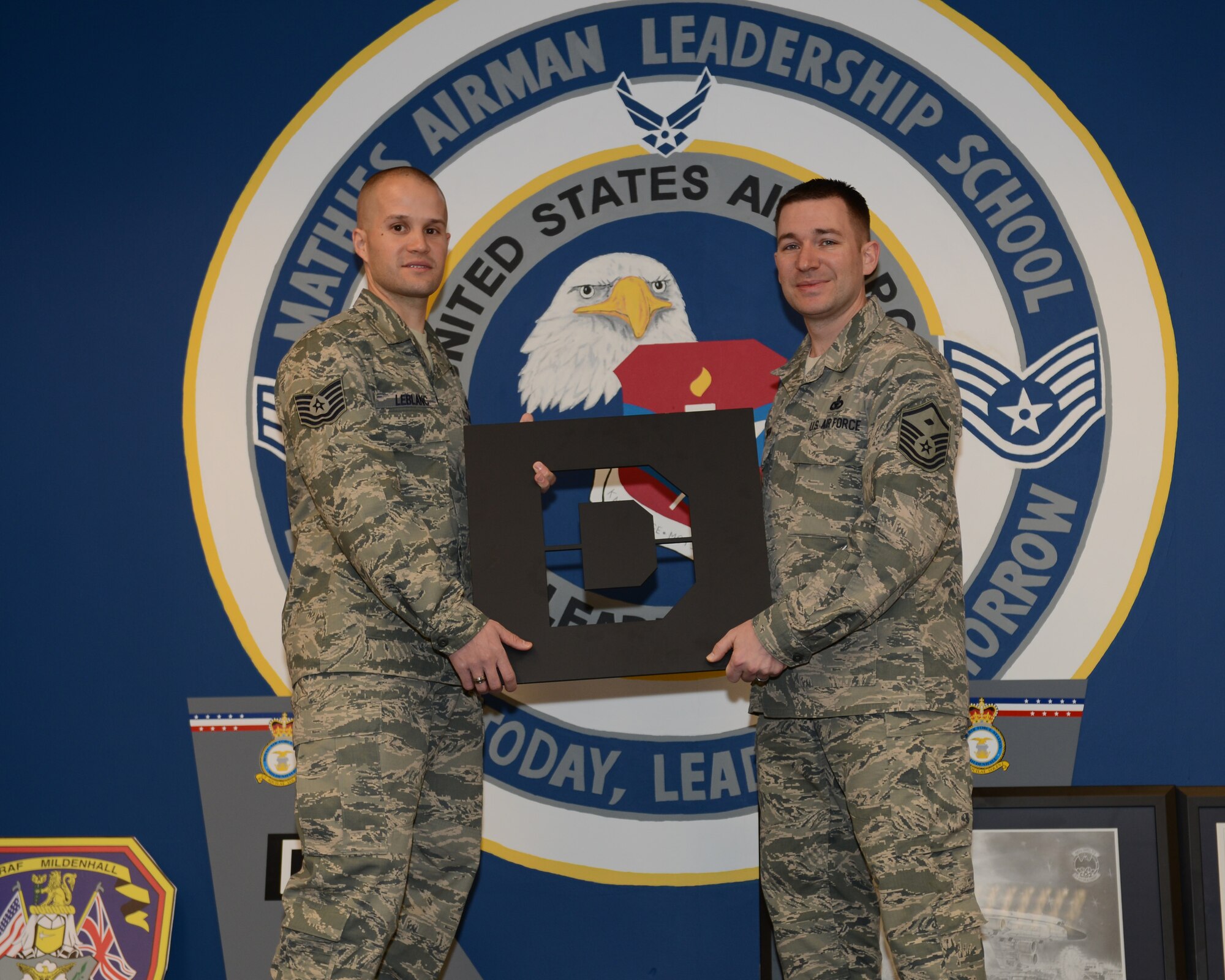 U.S. Air Force Master Sgt. Cody Green from Temperance, Mich., 95th Reconnaissance Squadron first sergeant, presents memorabilia to U.S. Air Force Tech. Sgt. Joshua Leblanc, Mathies Airman Leadership School acting commandant from Houston, on behalf of the Team Mildenhall Top 3 Feb. 14, 2014, on RAF Feltwell, England. The Top 3 met the need to bring heritage items to the 100th Air Refueling Wing, Flight Room in Mathies ALS as a way to inspire the students attending the school. The organization, comprised of enlisted service members at the rank of master sergeant or higher, donated Square D decor and coordinated a volunteer force to repaint various rooms in the schoolhouse. (U.S. Air Force photo by Airman 1st Class Preston Webb/Released)