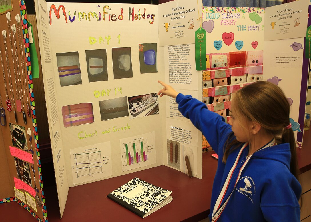 Kadence Hernandez, 8-years-old, daughter of Master Gunnery Sgt. Carlos Hernandez, operations chief, Marine Corps Communication-Electronics school, presents her project of hotdog mumification at Condor Elementary School's Science Night Feb. 5, 2014. The project involves mumifying a hotdog by burying it in baking soda and checking moisture levels after three days. 