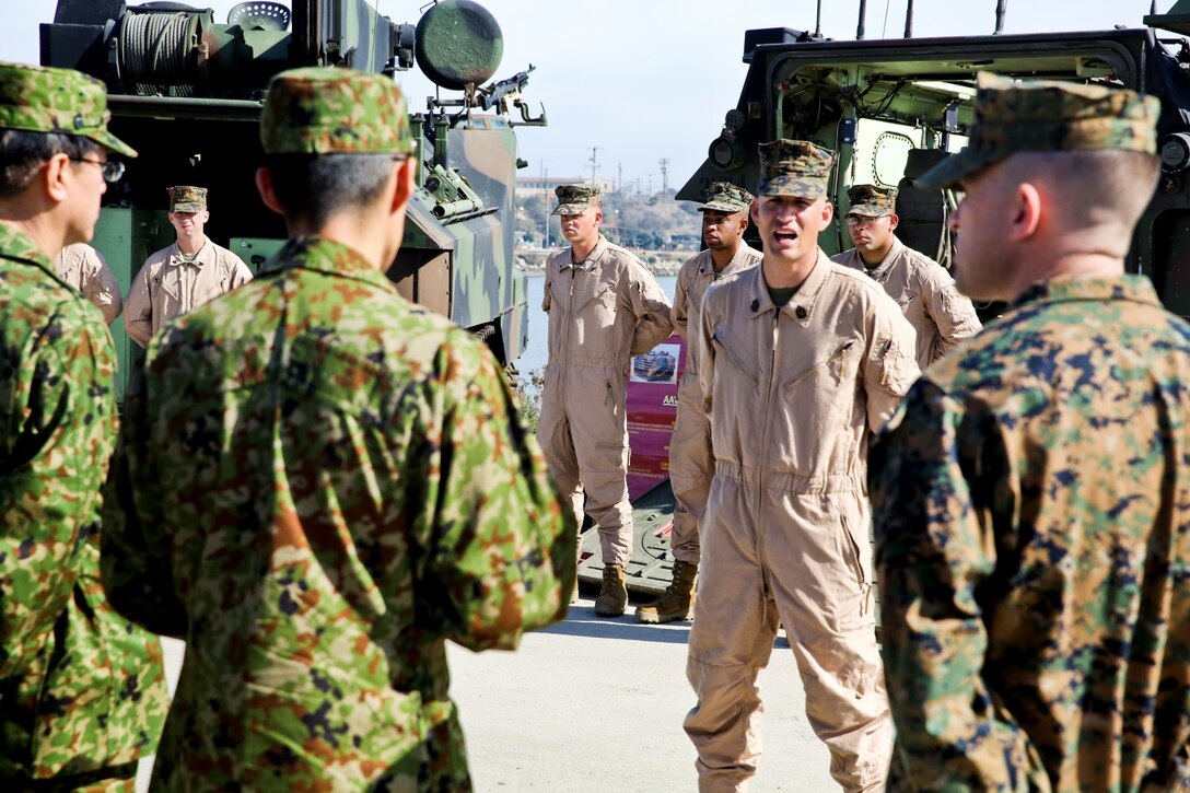 U.S. Marine Gunnery Sgt. Daryl Lee, middle, platoon sergeant, 3rd Assault Amphibian Battalion, welcomes U.S. Marine officers and officials from the Japan Ground Self-Defense Force to a splash demonstration with AAV-7 Assault Amphibious Vehicles during Exercise Iron Fist 2014 aboard Camp Pendleton, Calif., Feb. 16, 2014. Iron Fist is an amphibious exercise that brings together Marines and sailors from the 15th Marine Expeditionary Unit, other I Marine Expeditionary Force units, and soldiers from the JGSDF, to promote military interoperability and hone individual and small-unit skills through challenging, complex and realistic training. (U.S. Marine Corps photo by Lance Cpl. Ricardo Hurtado/Released)