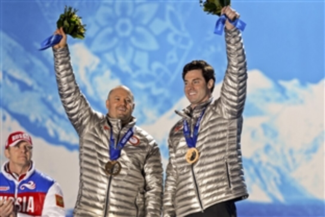 Former U.S. Army World Class Athlete Program bobsledder Steven Holcomb of Park City, Utah, and Steve Langton of Melrose, Mass., hoist the flowers and display their bronze medals during the Olympic two-man bobsled medal ceremony at Olympic Park in Sochi, Russia, Feb. 18, 2014.