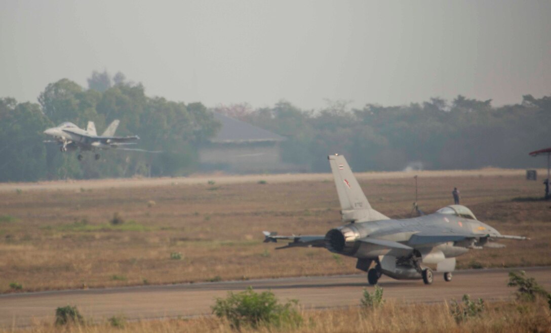 An FA-18D Hornet aircraft takes off as a Thai F-16 waits to take off from Wing One Royal Thai Air Force Base, Nakhon Ratchasima, Kingdom of Thailand, Feb. 19 during Exercise Cobra Gold 2014. CG 14 is a joint, multinational exercise conducted annually in the Kingdom of Thailand aimed at enhancing and increasing multinational interoperability. The FA-18D Hornet is with Marine All Weather Fighter Attack Squadron 242, Marine Aircraft Group 12, 1st Marine Aircraft Wing, III Marine Expeditionary Force. The F-16 is with Squadron 103, Wing One, Royal Thai Air Force. 
