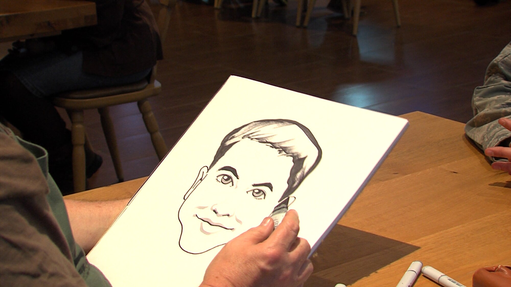 A cartoonist from the National Cartoonist Society sketches an Airman during a United Services Organization event Feb. 10, 2014, Ramstein Air Base, Germany. The National Cartoonist Society is an association that has been drawing sketches and raising morale in the military since World War II. (Courtesy photo)