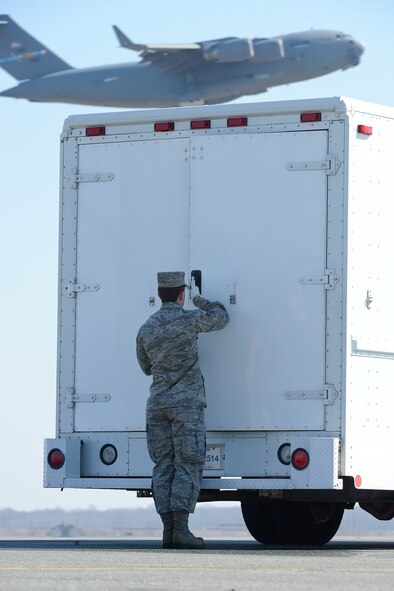 Senior Airman Tyler Wright secures the doors of a transfer vehicle during a dignified transfer for U.S. Marine Corps Master Sgt. Aaron C. Torian, while a C-17A Globemaster III from the 436th Airlift Wing is captured in-flight in the background,  Feb. 18, 2014, Dover Air Force Base, Del. Wright is assigned to the 911th Airlift Wing, Pittsburgh International Airport Air Reserve Station, Pa. and currently deployed to Air Force Mortuary Affairs Operations at Dover. Torian was assigned to 2nd Marine Special Operations Battalion, Marine Special Operations Regiment, U.S. Marine Corps Forces Special Operations Command, Camp Lejeune, N.C. (U.S. Air Force photo/Greg L. Davis)