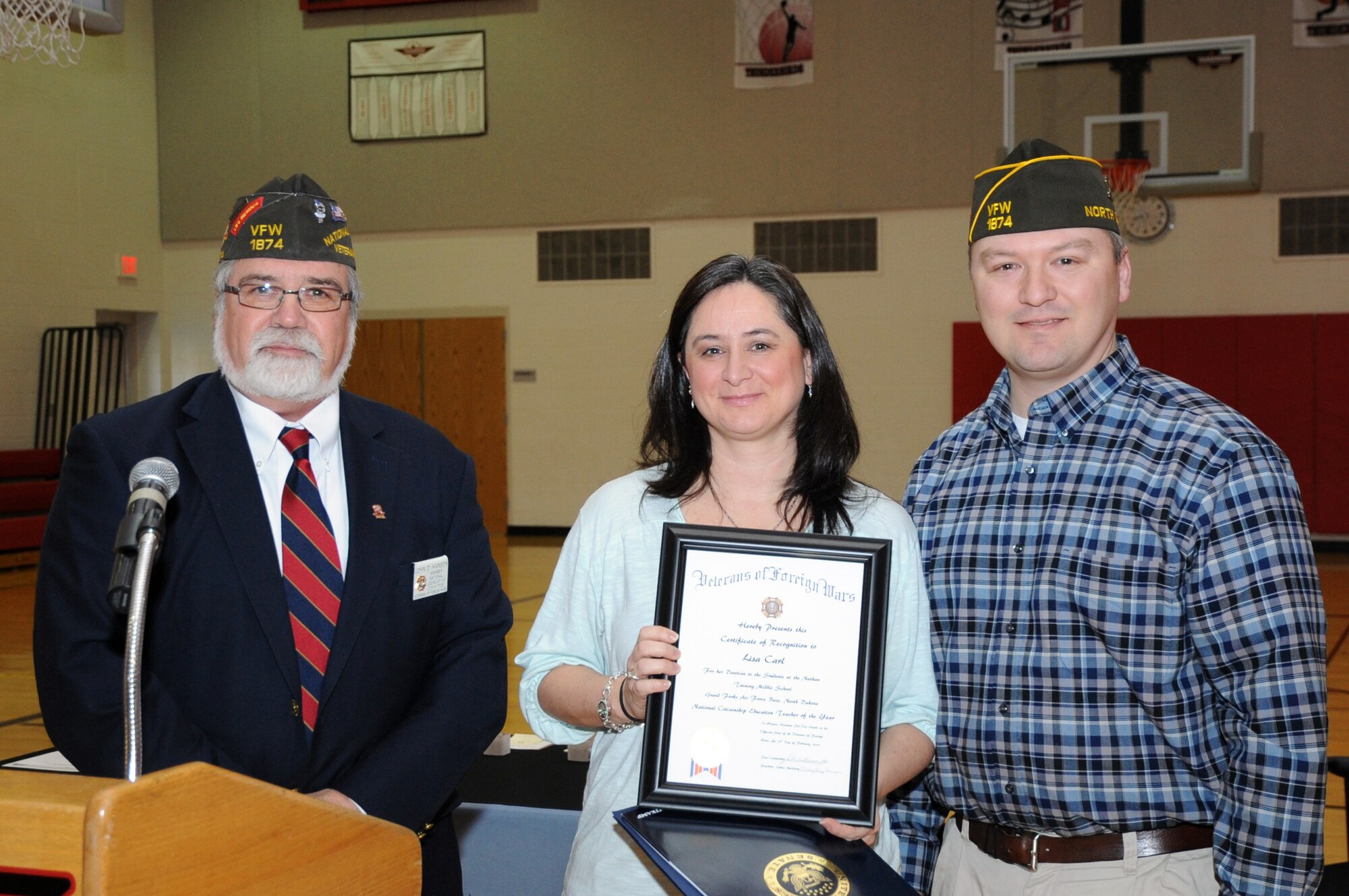 John Hanson (left), Grand Forks Veterans of Foreign Wars post commander, presents Lisa Carl and her husband Jeff with the VFW National Citizenship Education Teacher Award, Feb. 19, 2014, at Twining Elementary and Middle School on Grand Forks Air Force Base, N.D. Mrs. Carl, a 6th grade teacher at the school, won the award at the state level and is currently competing at the national level. (U.S. Air Force photo/Staff Sgt. David Dobrydney)