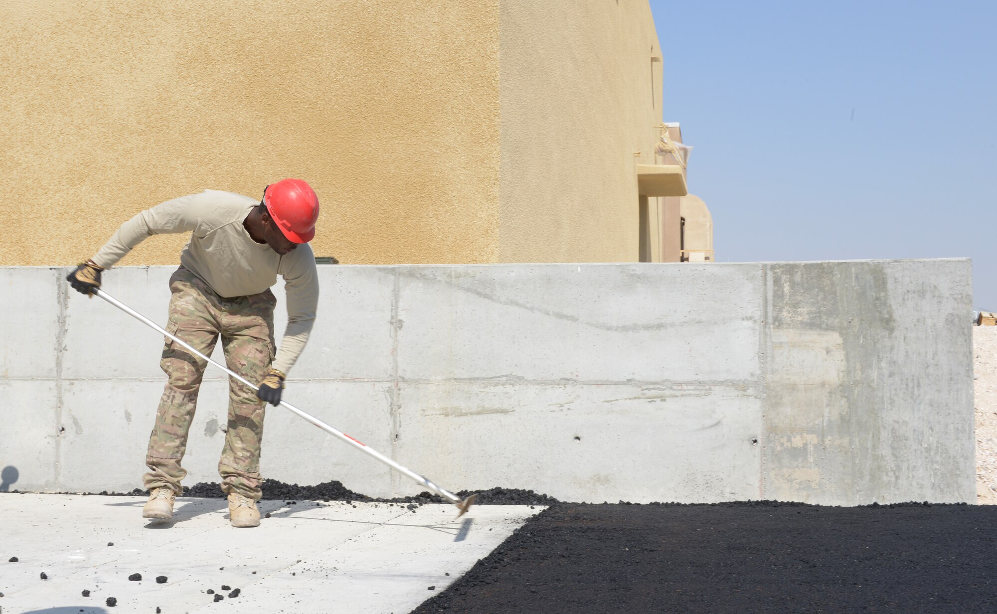 Senior Airman Jason Collins rakes new asphalt at Al Udeid Air Base, Qatar, Feb. 19, 2014. The asphalt will be paved into an access road for the newly built Contingency Aeromedical Staging Facility. The CASF will house and provide medical care to wounded service members prior to medical evacuation. RED HORSE provides heavy repair and construction capabilities throughout the U.S. Air Forces Central Command area of responsibility. Collins is a 557th Expeditionary Rapid Engineer Deployable Heavy Operational Repair Squadron Engineer heavy equipment operator deployed from Nellis Air Force Base, Nev., and a Warner Robins, Ga., native. (U.S. Air Force photo/Senior Airman Hannah Landeros)