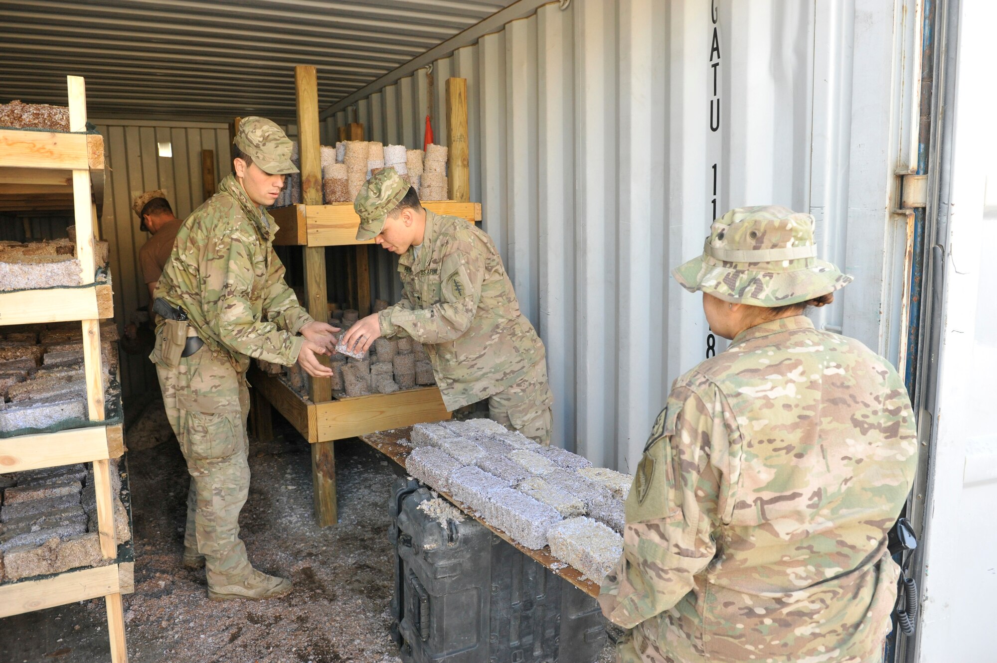 U.S. Service members unload newly formed fire bricks and place them on racks for drying at Camp Phoenix, Afghanistan, Feb. 16, 2014. The Service members all volunteered to make the fire starters that are later distributed to local Afghan families to use as a source of heat during cold weather.(U.S. Air Force photo by Senior Master Sgt. Gary J. Rihn/Released)
