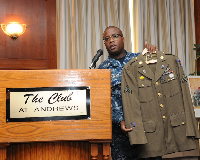 Guest speaker Lt. Cmdr. Bryan Pettigrew holds up his father’s Army Air Corps uniform at the club at Joint Base Andrews, Md., on Feb. 19, 2014, as he explains the challenges his father faced during segregation. Pettigrew is the Navy Information Dominance Corps., Region of Washington, D.C. assistant officer in charge. (U.S. Air Force photo/Airman 1st Class Ryan J. Sonnier)