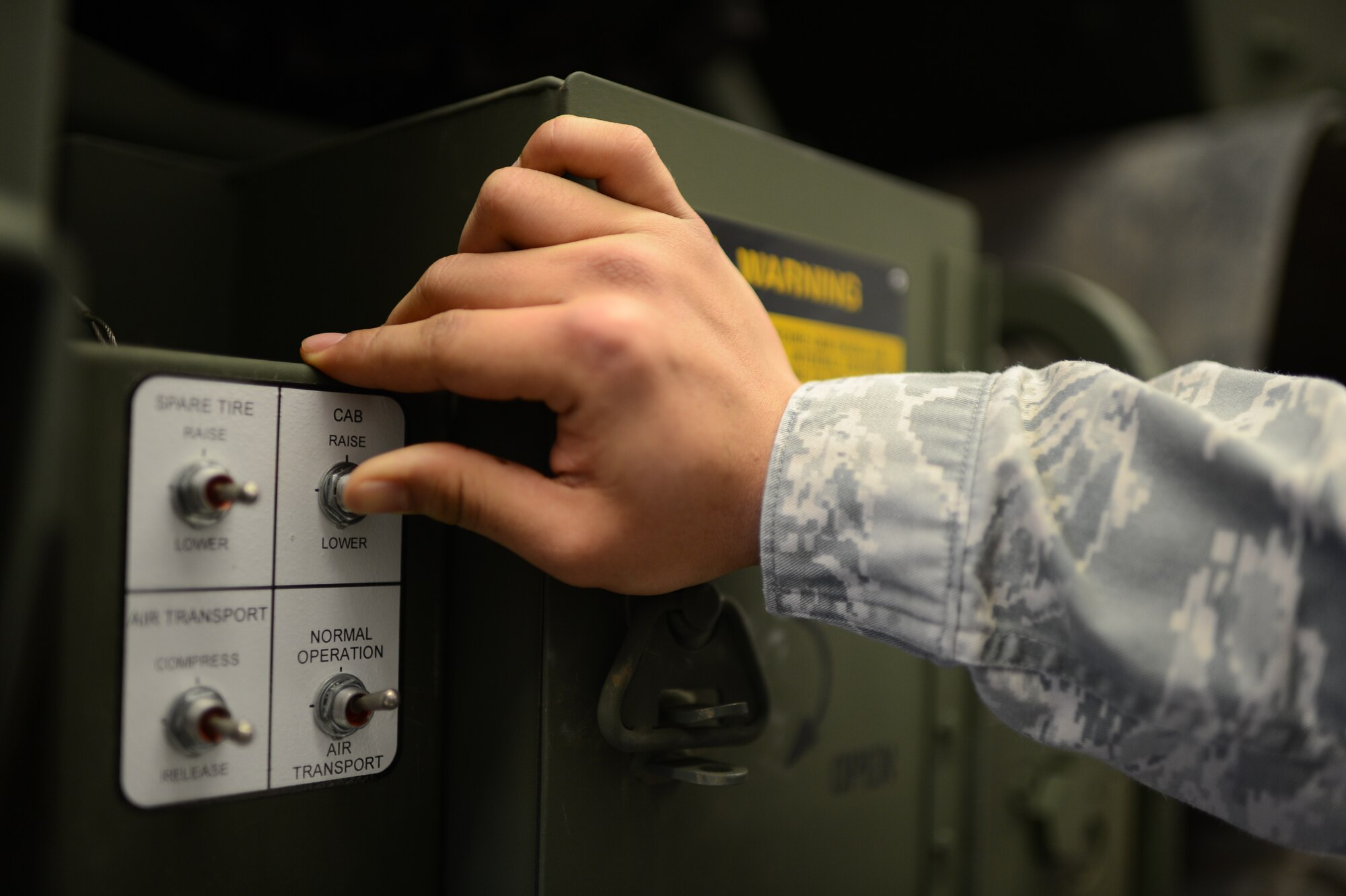 U.S. Air Force Airman 1st Class Evin Diaz, 606th Air Control Squadron vehicle maintenance technician from Guam, presses a lift button on a five-ton troop carrier vehicle on Spangdahlem Air Base, Germany, Feb. 20, 2014. The cab must be lifted to give maintenance technicians access to the vehicle’s engine components. (U.S. Air Force photo by Senior Airman Gustavo Castillo/Released)