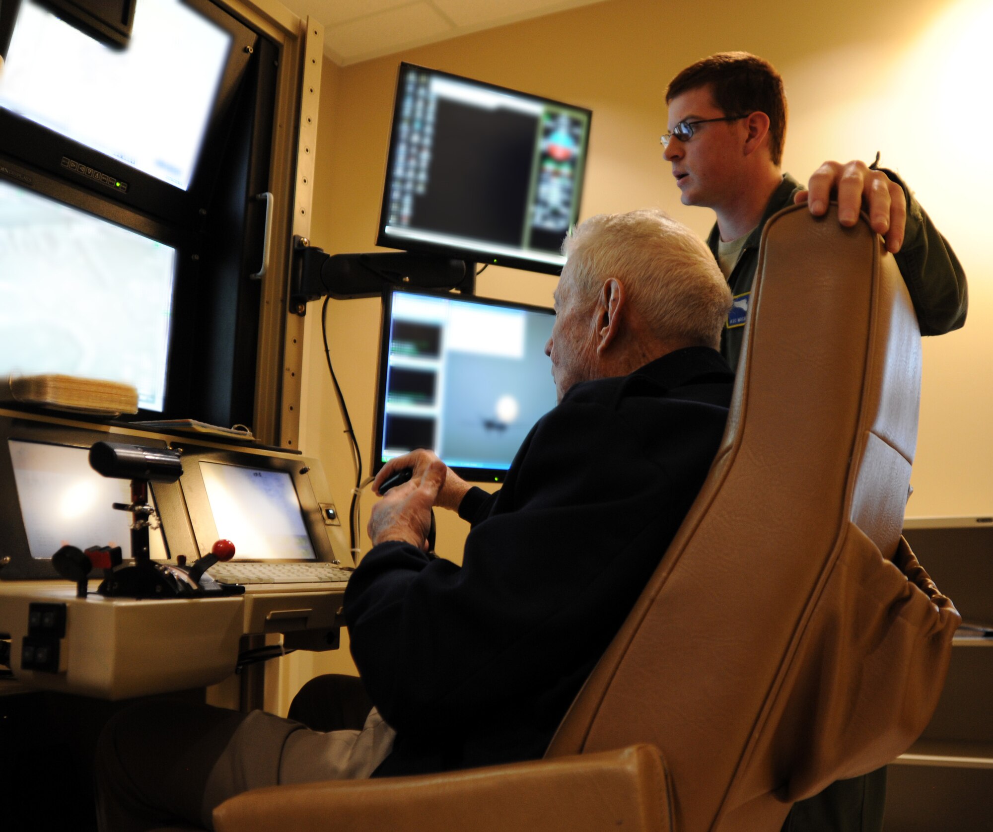 Retired Chief Master Sgt. of the Air Force Robert Gaylor, front, learns to fly a remotely piloted aircraft using a flight training simulator Feb. 7, 2014, during a visit to the 432nd Wing, 432nd Air Expeditionary Wing. During his visit, Gaylor commented on the high degree of professionalism exhibited by the Airmen he met. (Portions of this image have been edited for security reasons.) (U.S. Air Force photo illustration /1st Lt S.S.)