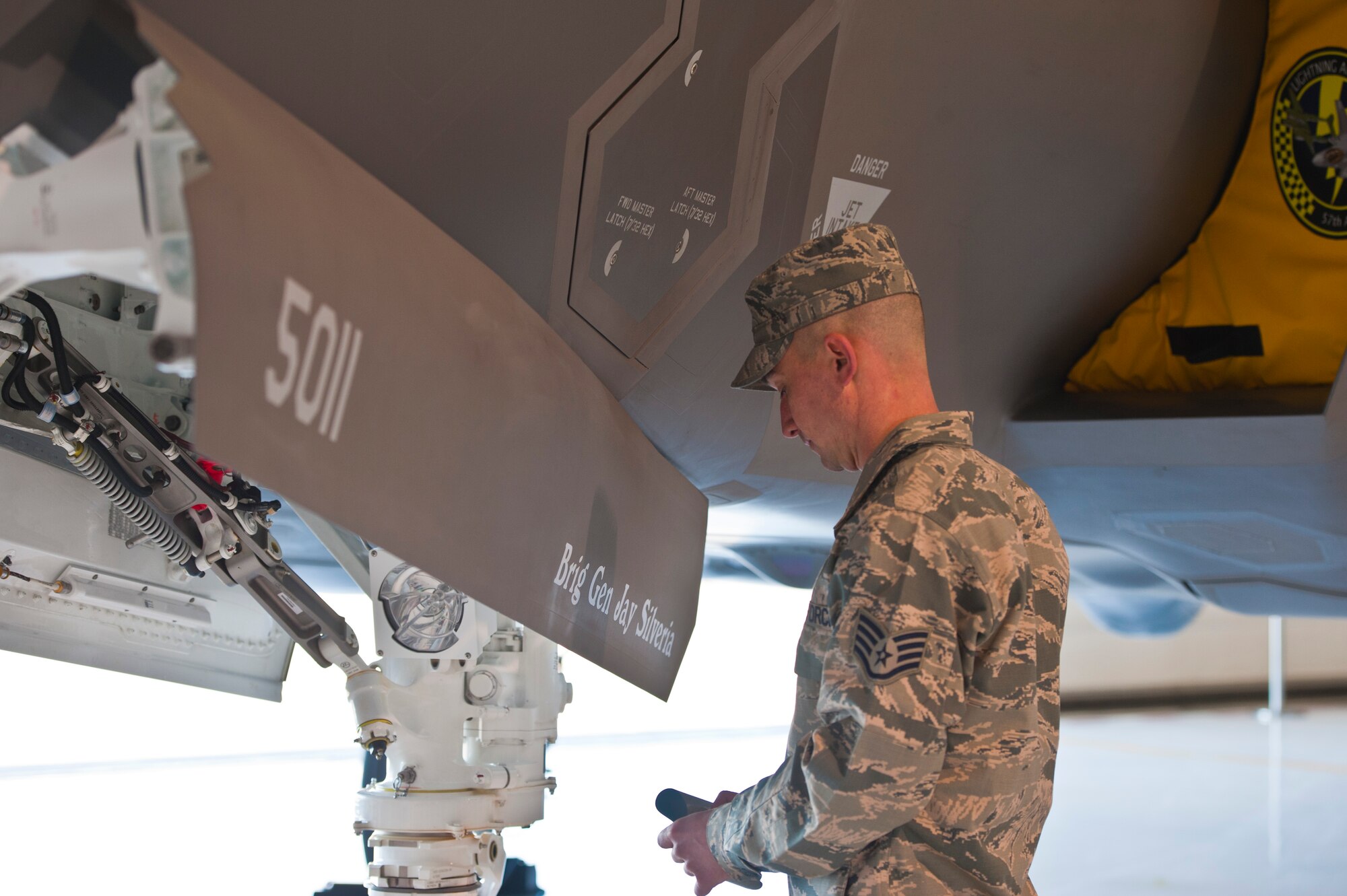 U.S. Air Force Staff Sgt.William Rispoli, 57th Aircraft Maintenance Squadron Lightning Aircraft Maintenance Unit dedicated crew chief, unveils Brig. Gen. Jay Silveria's name on an F-35 Lightning II during an assumption of command ceremony in the Thunderbird hangar Feb. 21, 2014, at Nellis Air Force Base, Nev. The F-35 will serve as Silveria’s flagship aircraft during his command at the U.S. Air Force Warfare Center.  (U.S. Air Force photo by Senior Airman Christopher Tam)