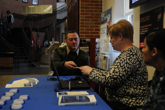 Lt. Col. Erik Arrington enrolls in the Pharmacy Home Delivery program with the help of Express Scripts representative Anissa Toenjes on Feb. 12, 2014, at Naval Health Clinic Quantico, as Petty Officer 2nd Class Zary Rivera, one of the clinic’s pharmacy technicians, looks on. 