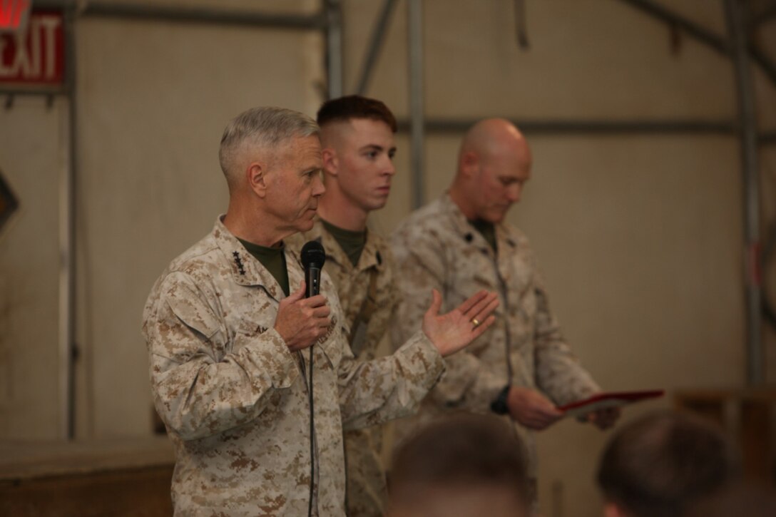 Jacob Schlauder, center, a corpsman with 1st Battalion, 9th Marine Regiment, is about to be awarded the Navy and Marine Corps Commendation Medal with a combat distinguishing device before a town hall meeting aboard Camp Leatherneck, Helmand province, Afghanistan, Feb. 18, 2014.  General Amos personally presented the medal with combat “V” to Schlauder, who despite suffering injuries himself, rendered medical aid to Marines who were injured in an attack when their vehicle was struck by an armor-piercing, rocket-propelled grenade while on patrol Jan. 25, 2014.