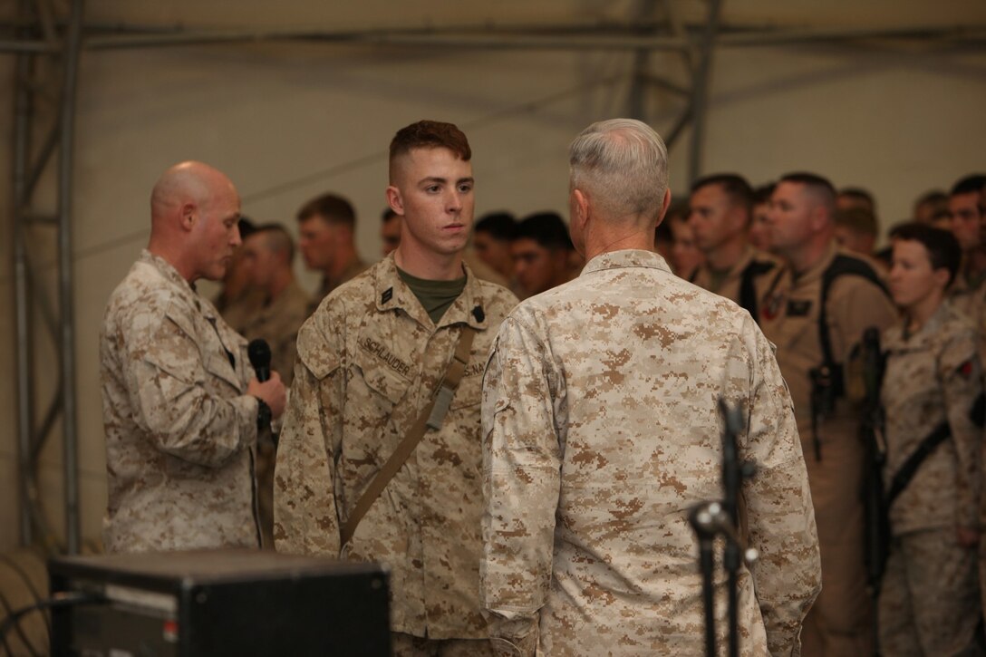 Seaman Jacob Schlauder, center, a corpsman with 1st Battalion, 9th Marine Regiment, stands before Gen. James F. Amos, commandant of the Marine Corps, as Sgt. Maj. Micheal P. Barrett, sergeant major of the Marine Corps, reads Schlauder’s Navy and Marine Corps Commendation Medal with a combat distinguishing device citation at a town hall meeting aboard Camp Leatherneck, Helmand province, Afghanistan, Feb. 18, 2014. General Amos personally presented the medal with combat “V” to Schlauder, who despite suffering injuries himself, rendered medical aid to Marines who were injured in an attack when their vehicle was struck by an armor-piercing, rocket-propelled grenade while on patrol Jan. 25, 2014.