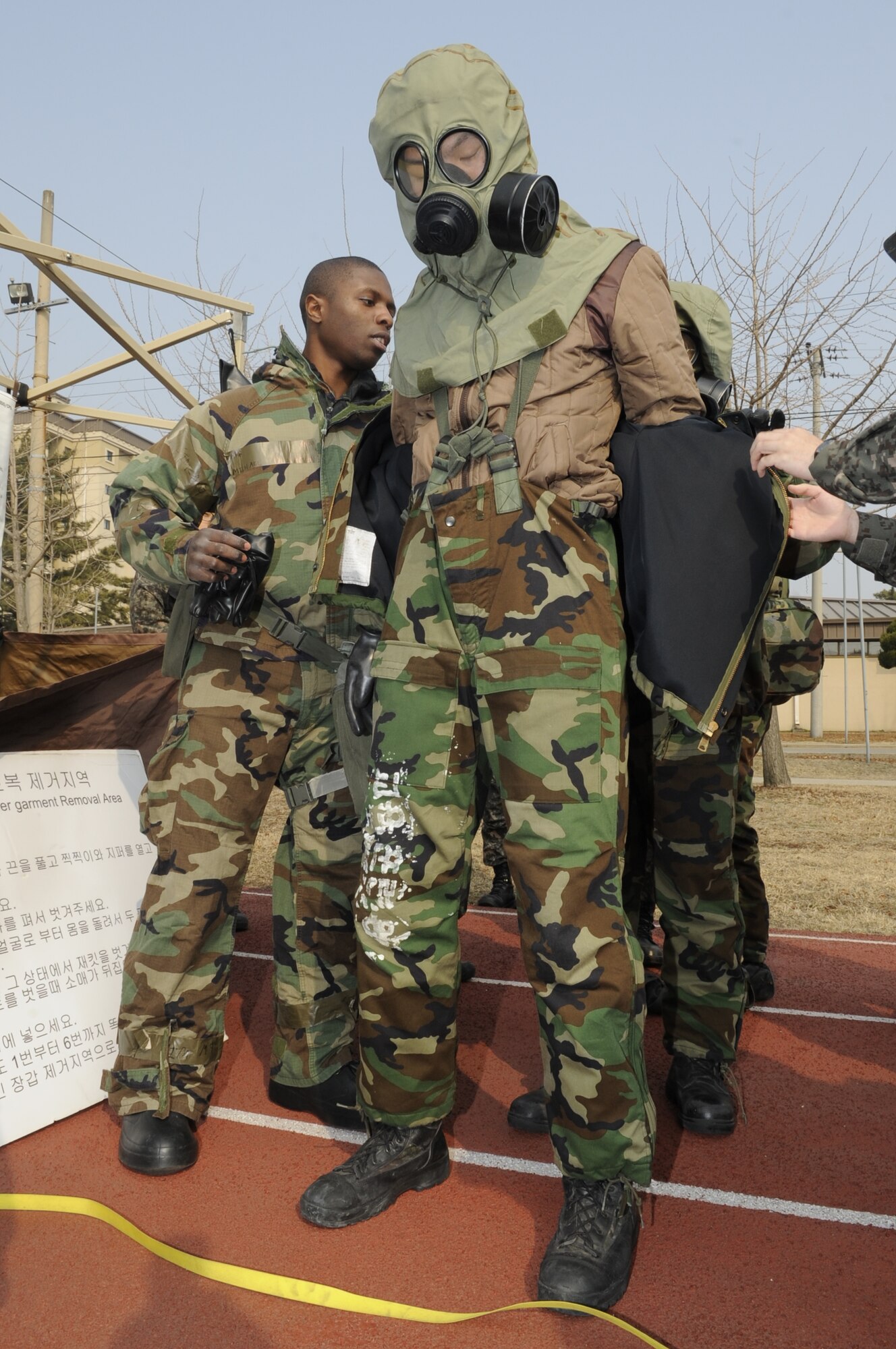 Senior Airman Michael Blackmon, 8th Civil Engineer Squadron journeyman, assists Republic of Korea airmen during the chemical, biological, radiological and nuclear training scenario, Feb. 24, 2014 at Kunsan Air Base, Republic of Korea. This particular station of the decontamination process required participants to remove their suits and dispose of them properly. (U.S. Air Force photo by Staff Sgt. Jessica Haas/Released)