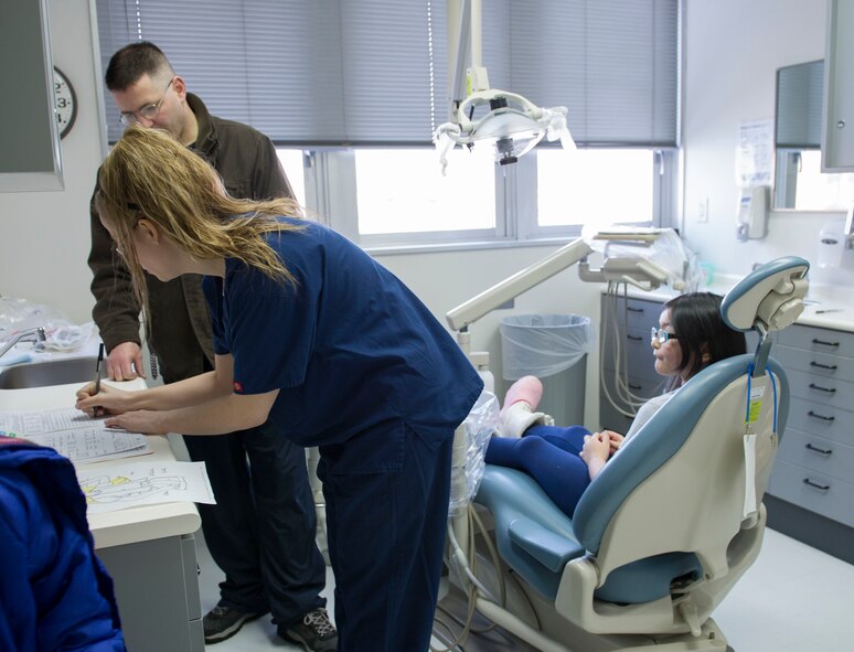 YOKOTA AIR BASE, Japan -- Senior Airman Christa Cooper, 374th Dental Squadron dental assistant, reviews paperwork for Tech. Sgt. Paul Pearson, 374th Maintenance Squadron and his daughter Andrea Pearson, for a routine dental exam during the Little Teeth-Big Smiles at Yokota Air Base, Japan, Feb. 22, 2014. As part of National Children's Dental Health Month, the 374 DS hosted walk-in clinic for children, including dental examinations, cleanings and education services. (U.S. Air Force photo by Staff Sgt. Andrea Salazar/Released)