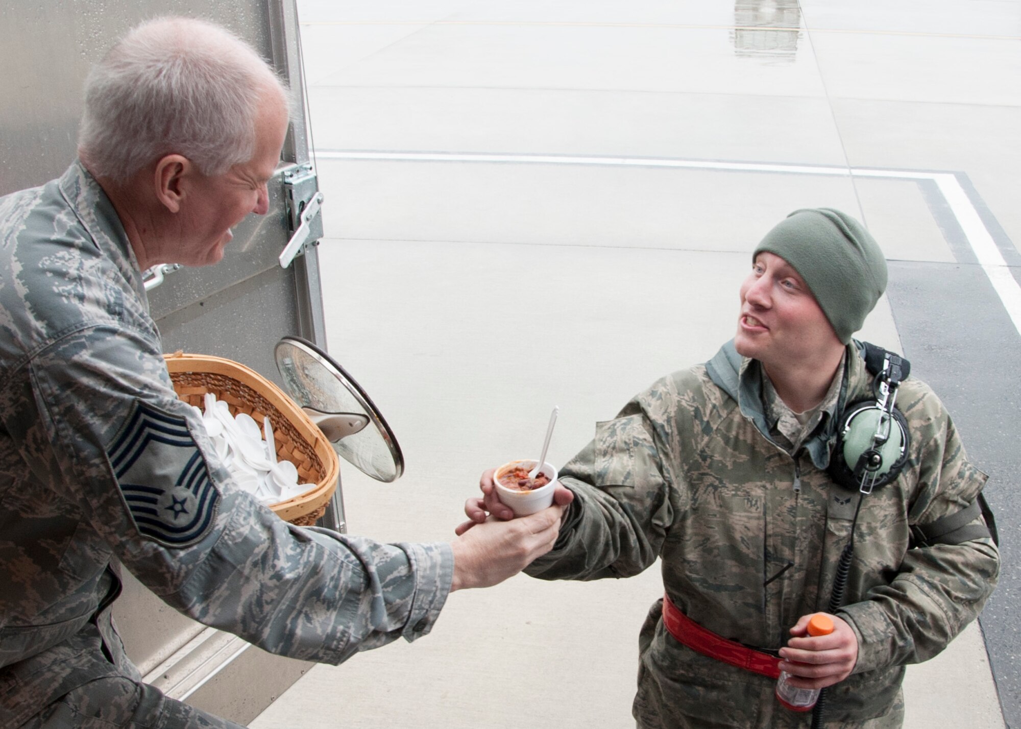 Chief Master Sgt. Richard Brackett, 436th Airlift Wing Chiefs Group, hands Airman1st Class Samuel Lieberman, 436th Aircraft Maintenance Squadron C-5M Super Galaxy crew chief, chili Feb. 19, 2014, Dover Air Force Base, Del. Chili and hot chocolate were passed out to help warm up the Airmen working in the wet and cold weather on the flight line. (U.S. Air Force photo/ Senior Airman Jared Duhon)