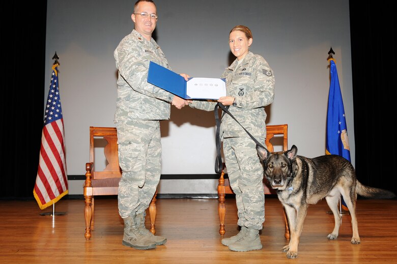 U.S. Air Force Staff Sgt. Alexandra Springman, 355th Security Forces Squadron, military working dog handler, accepts a certificate of meritorious service on behalf of Dexter, 5-years-old, 355th SFS military working dog, from Maj. Douglas Whitehead, 355th SFS commander, during his retirement ceremony at Davis-Monthan Air Force Base, Ariz., Feb. 19, 2014. Dexter has served as a patrol and explosive detection dog since joining the AF in October 2009. (U.S. Air Force photo by Airman 1st Class Chris Drzazgowski/Released) 